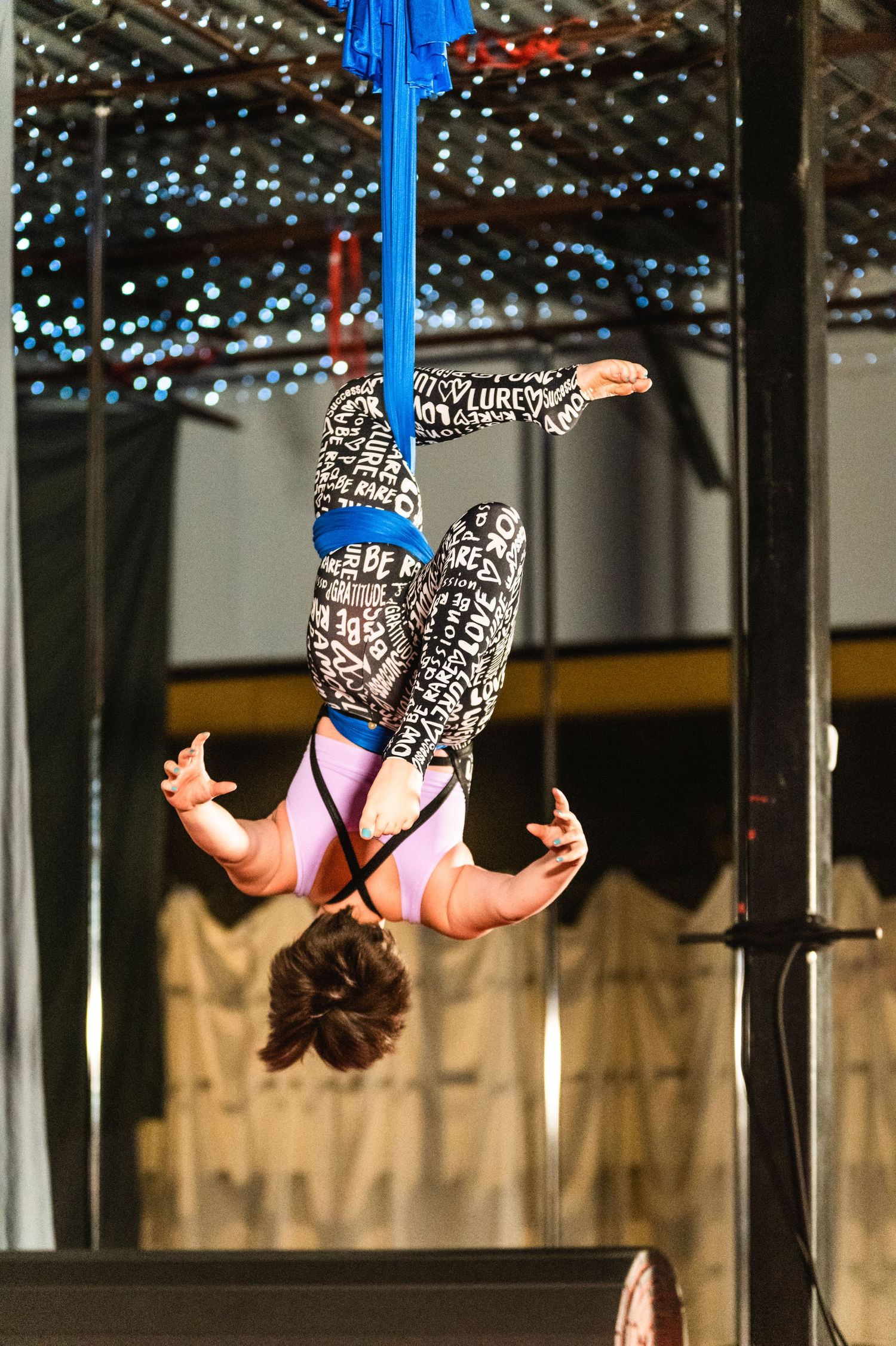 Aerial artist suspended upside down on blue silk performing intricate pose.