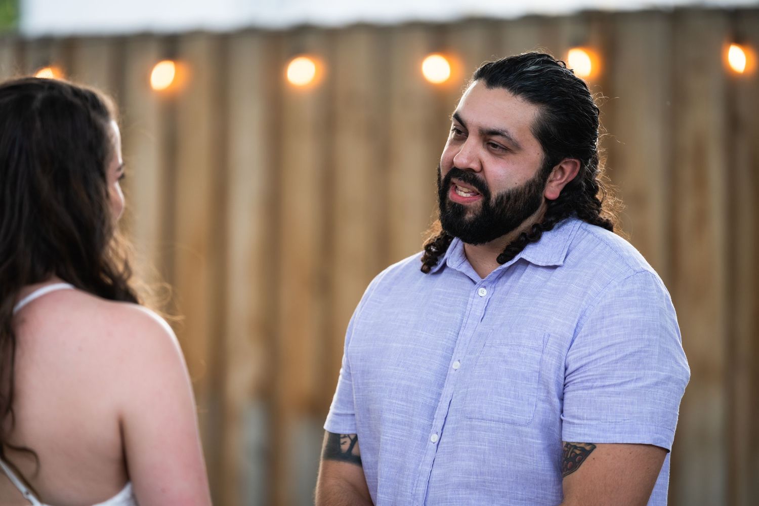 An outdoor conversation between two people with string lights and a wooden fence in the background.