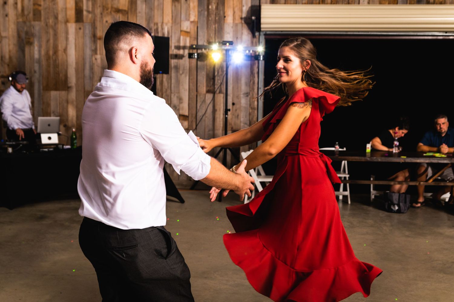 A couple dances energetically in a rustic venue, with the woman's red dress swirling dramatically.
