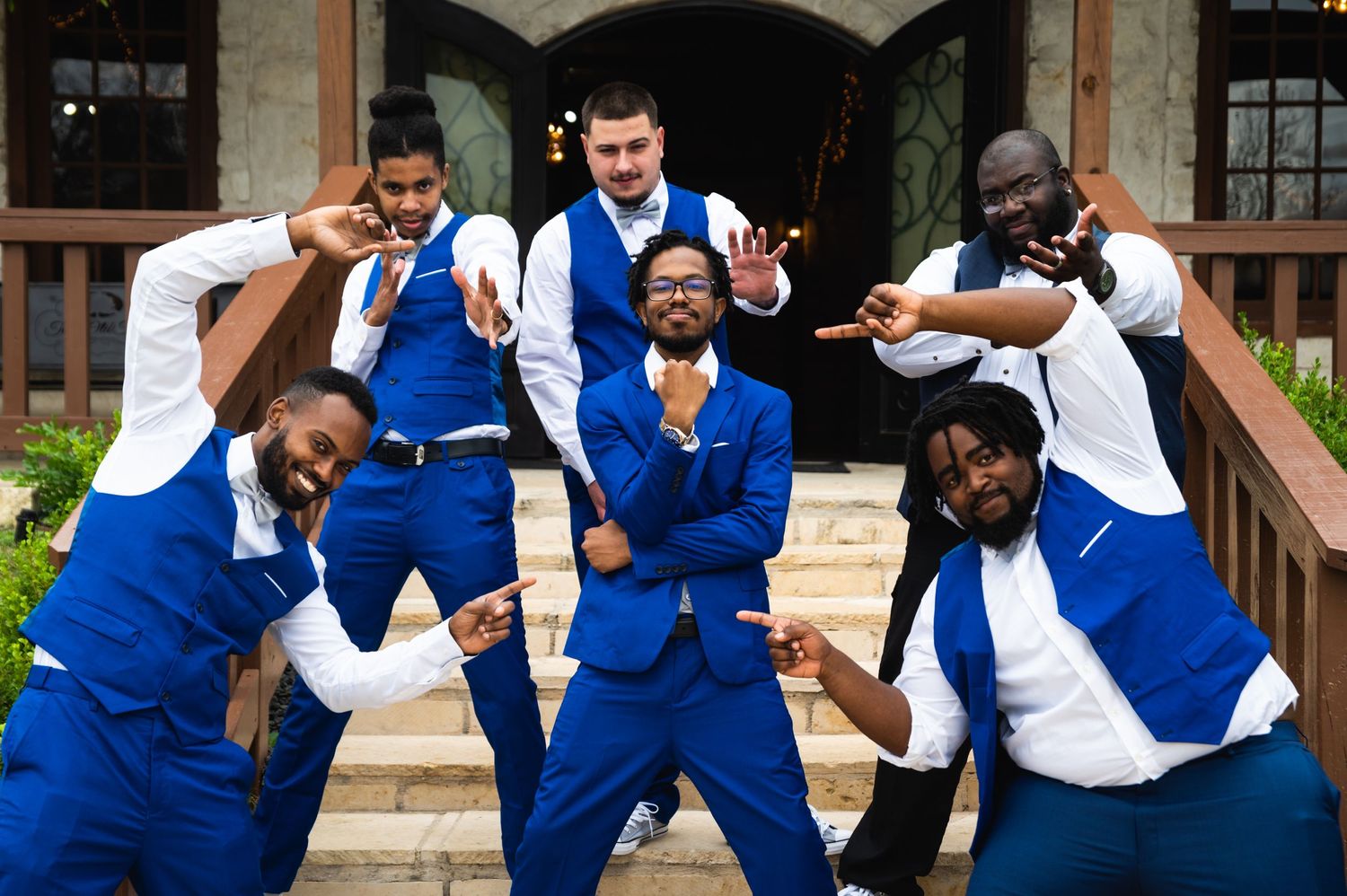 Wedding party in bright blue suits strikes fun poses on outdoor steps.