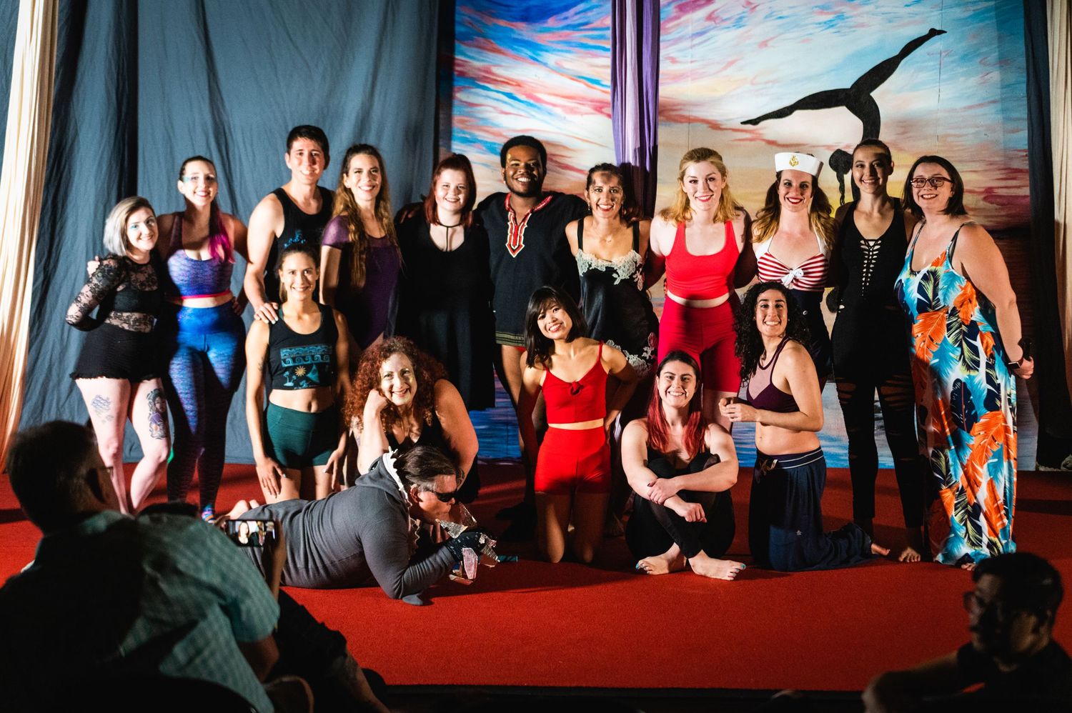 A group photo of aerial performance artists posing together on a red stage.