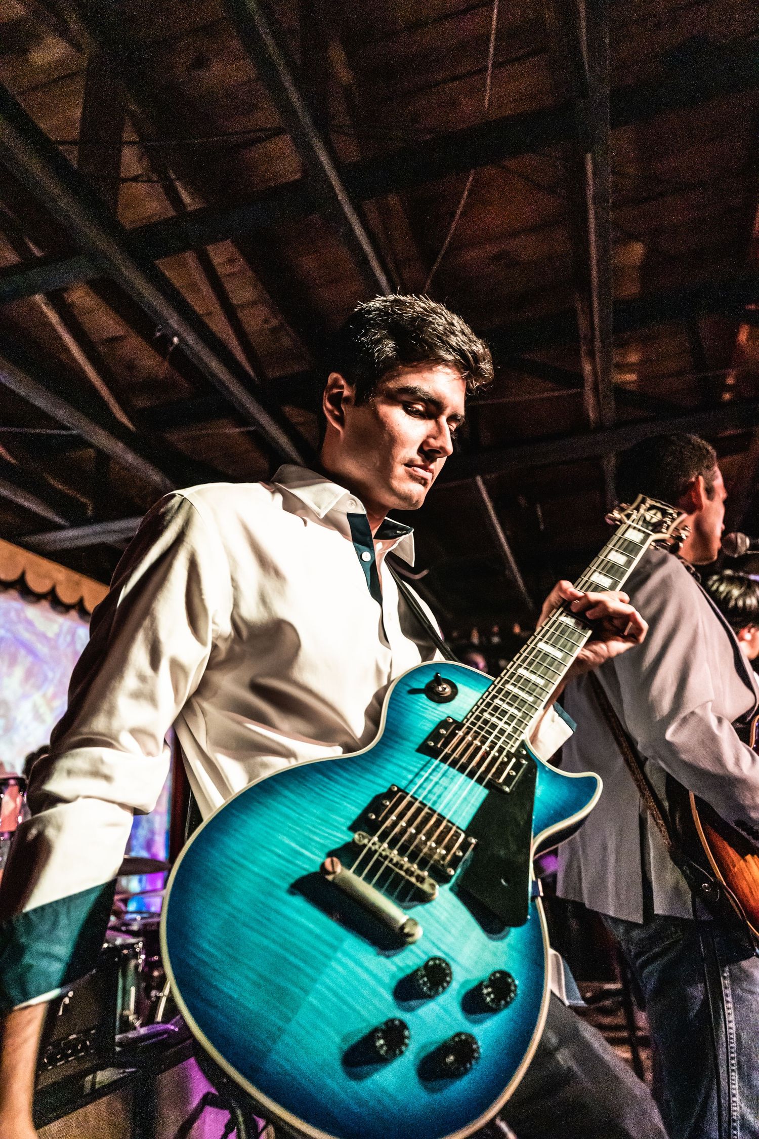Musician playing a turquoise electric guitar on stage under dramatic lighting.