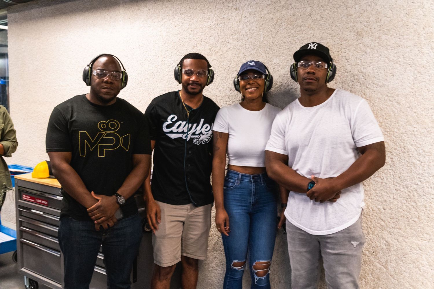 Four friends pose together against a plain wall during an indoor event.