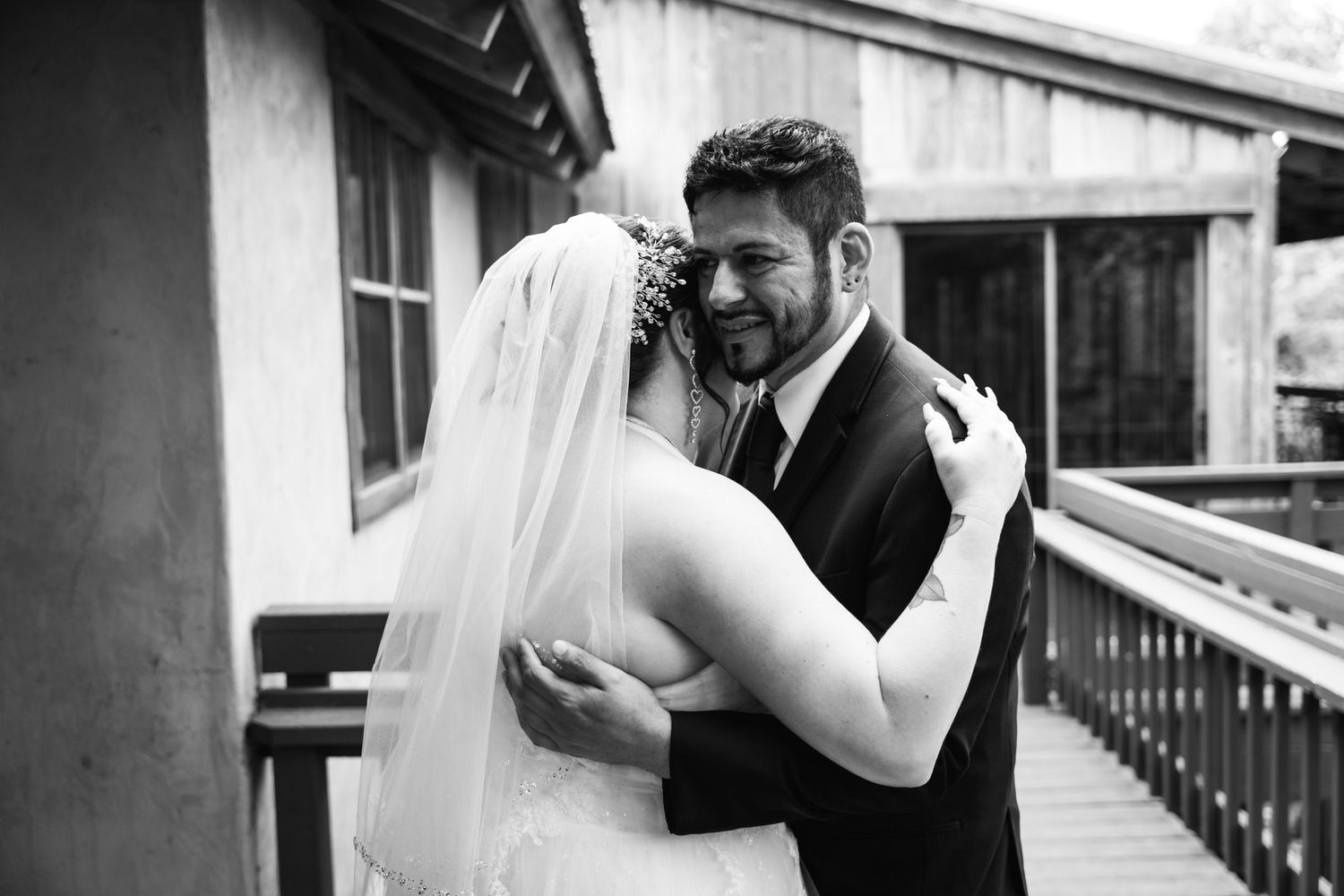 A black and white photo captures an intimate moment between newlyweds on a covered porch.