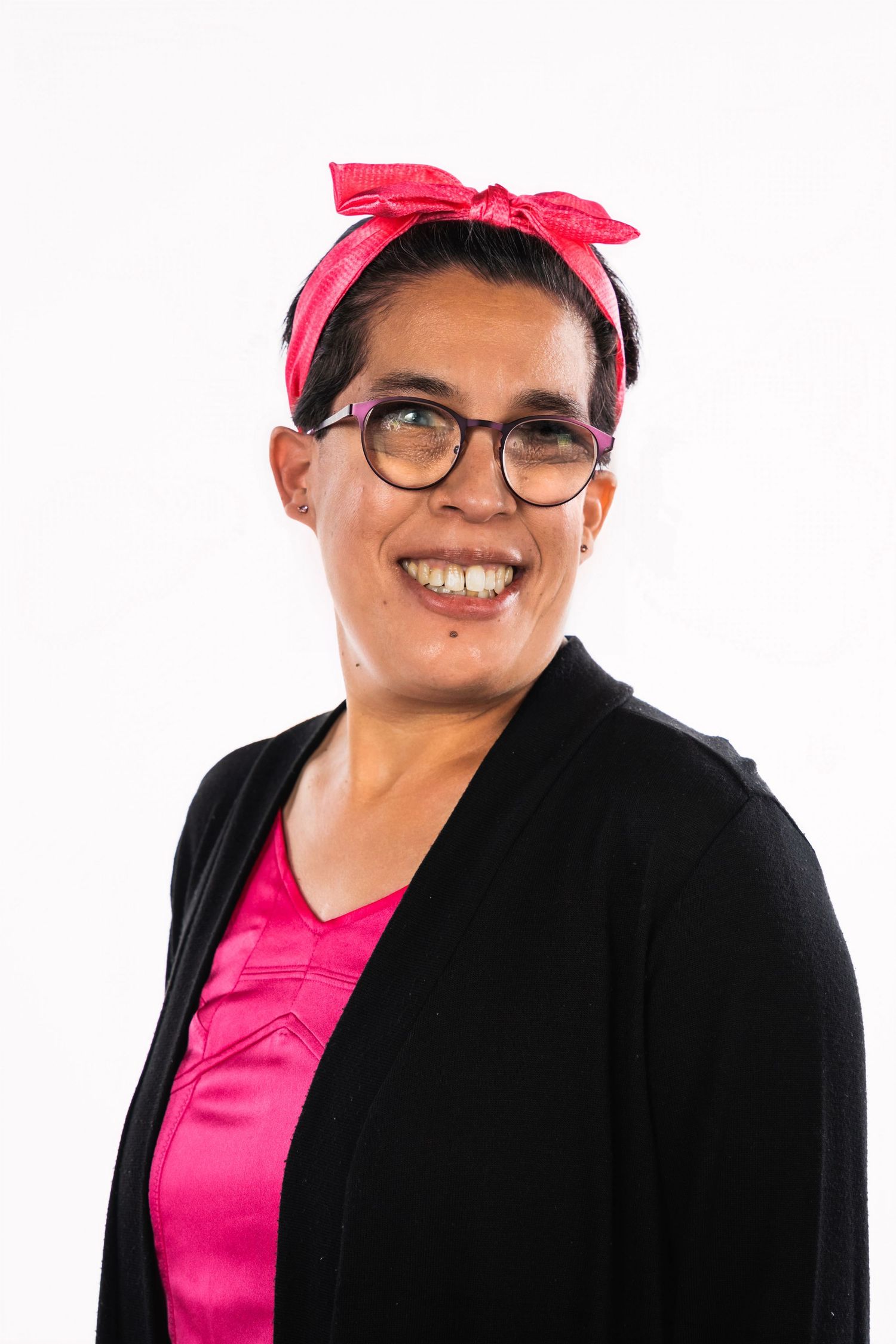 A person wearing a pink headband, glasses and black cardigan against a white background.