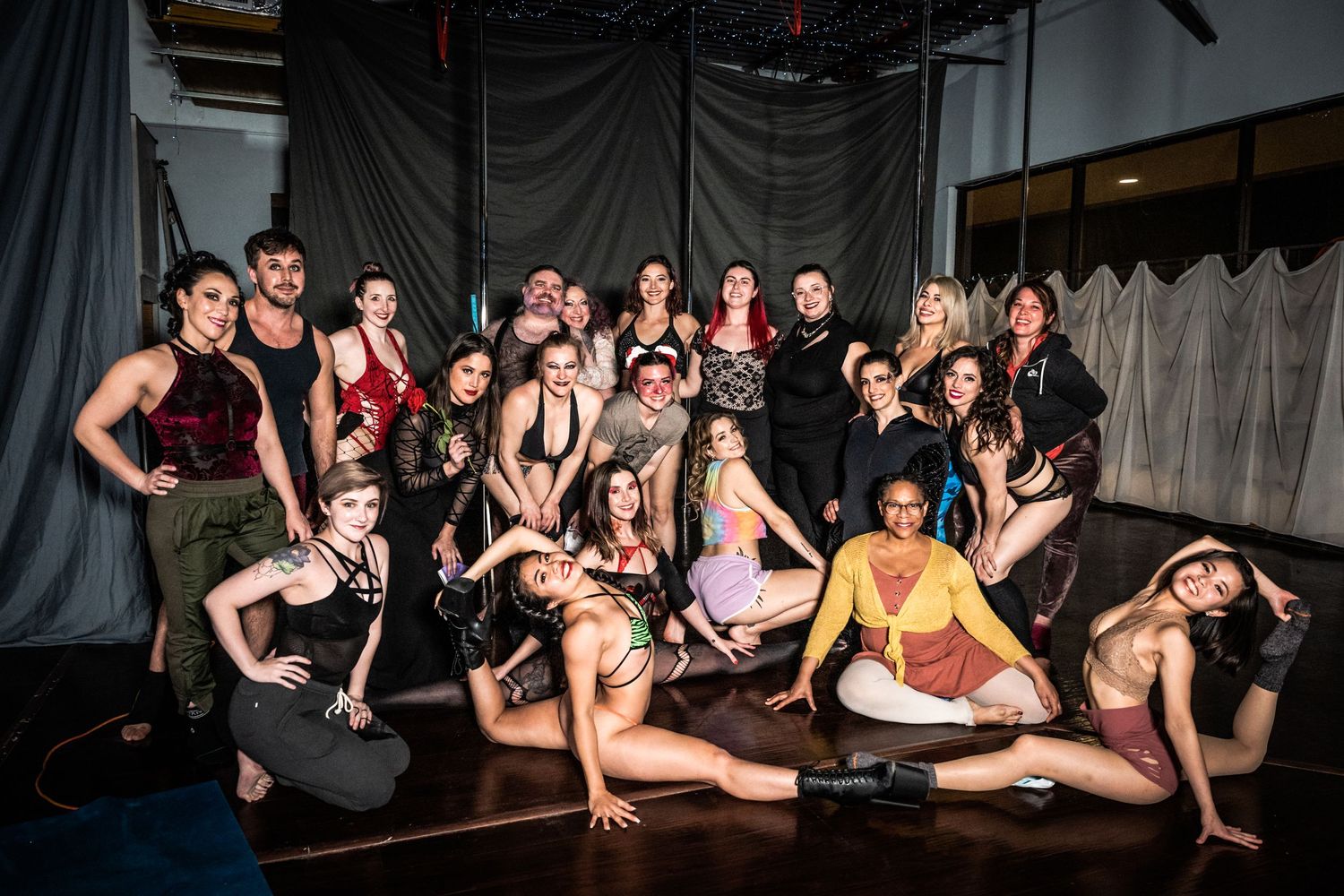 Group of performers striking dramatic poses in theatrical costumes against grey backdrop.