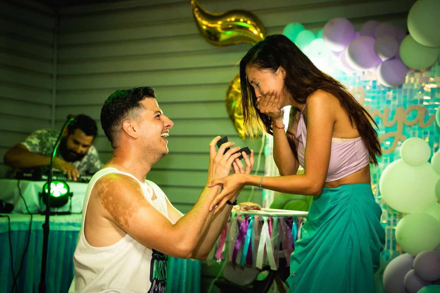 A romantic proposal scene with decorative balloons and lighting at an outdoor party setting.