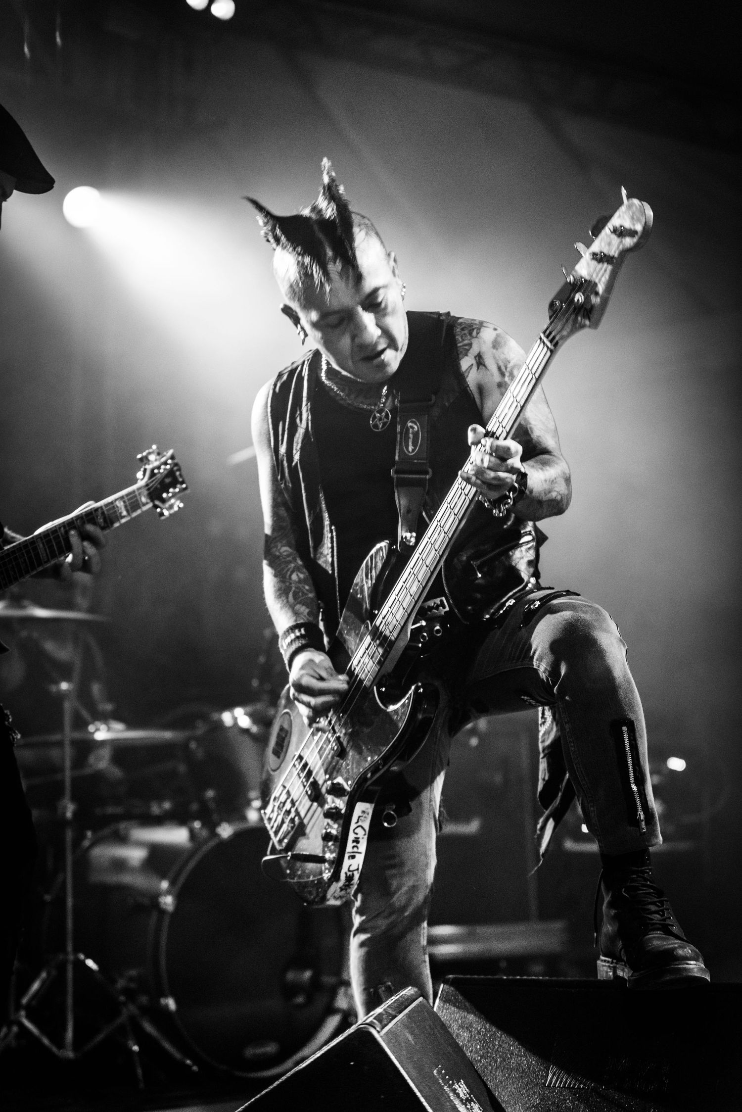 Bass guitarist performs energetic stance on stage in dramatic black and white concert photo.