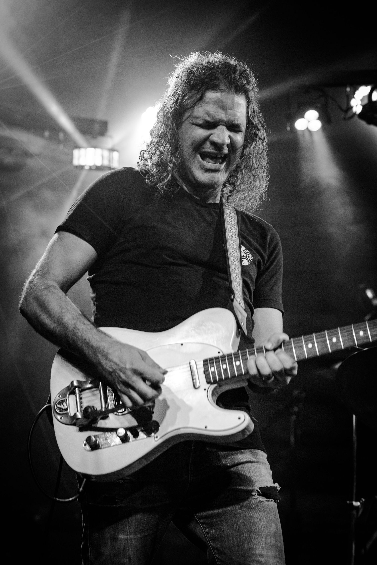 Energetic musician playing white electric guitar on stage under dramatic concert lighting.