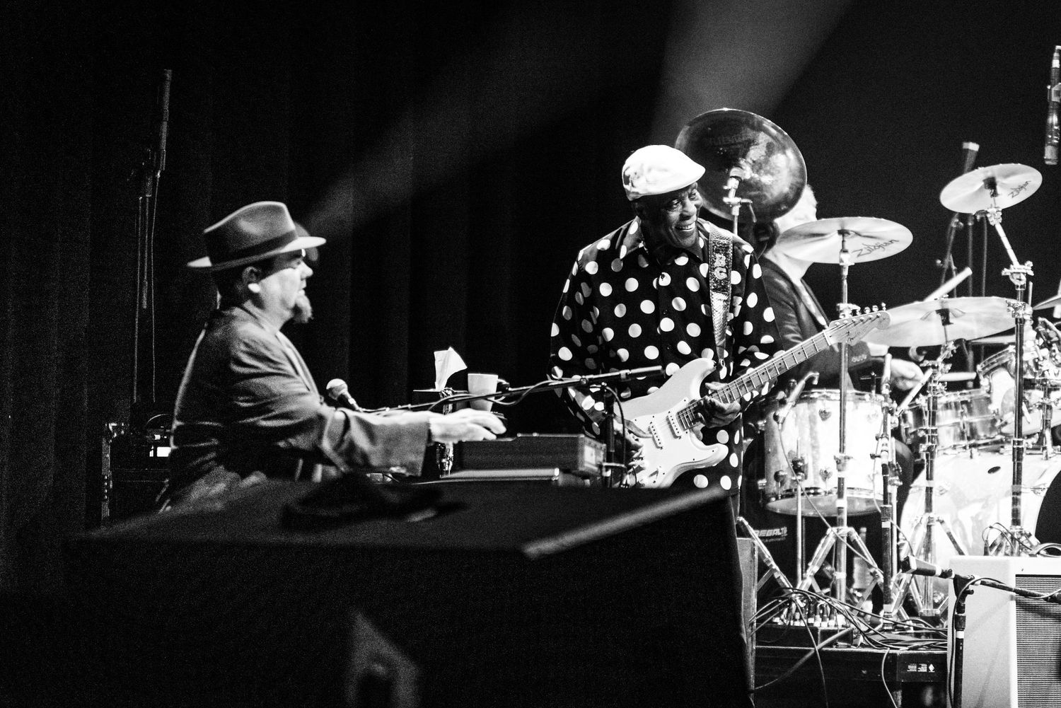 Black and white image of musicians performing with keyboard and drums on a concert stage.