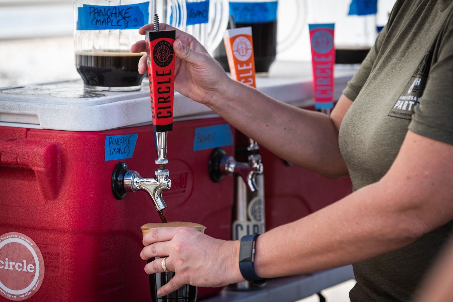 Hands pouring a draft beer from a red keg tap system.