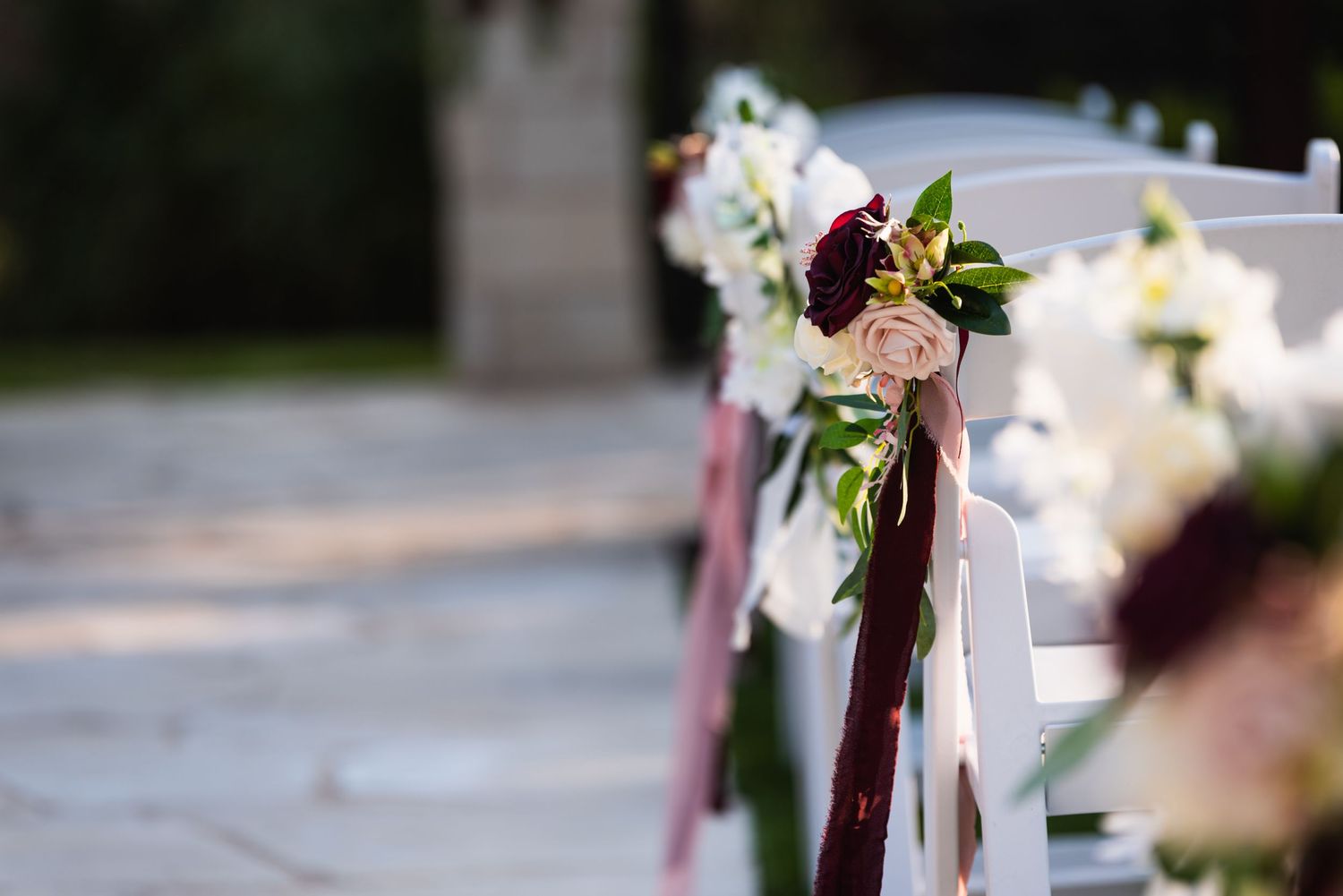 Wedding aisle decorated with pink flowers and burgundy ribbons on chairs.