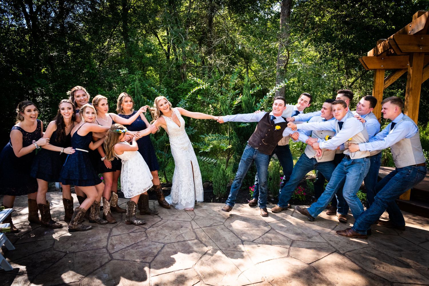 Wedding party poses for a fun group photo with dramatic leaning pose outdoors on stone patio.