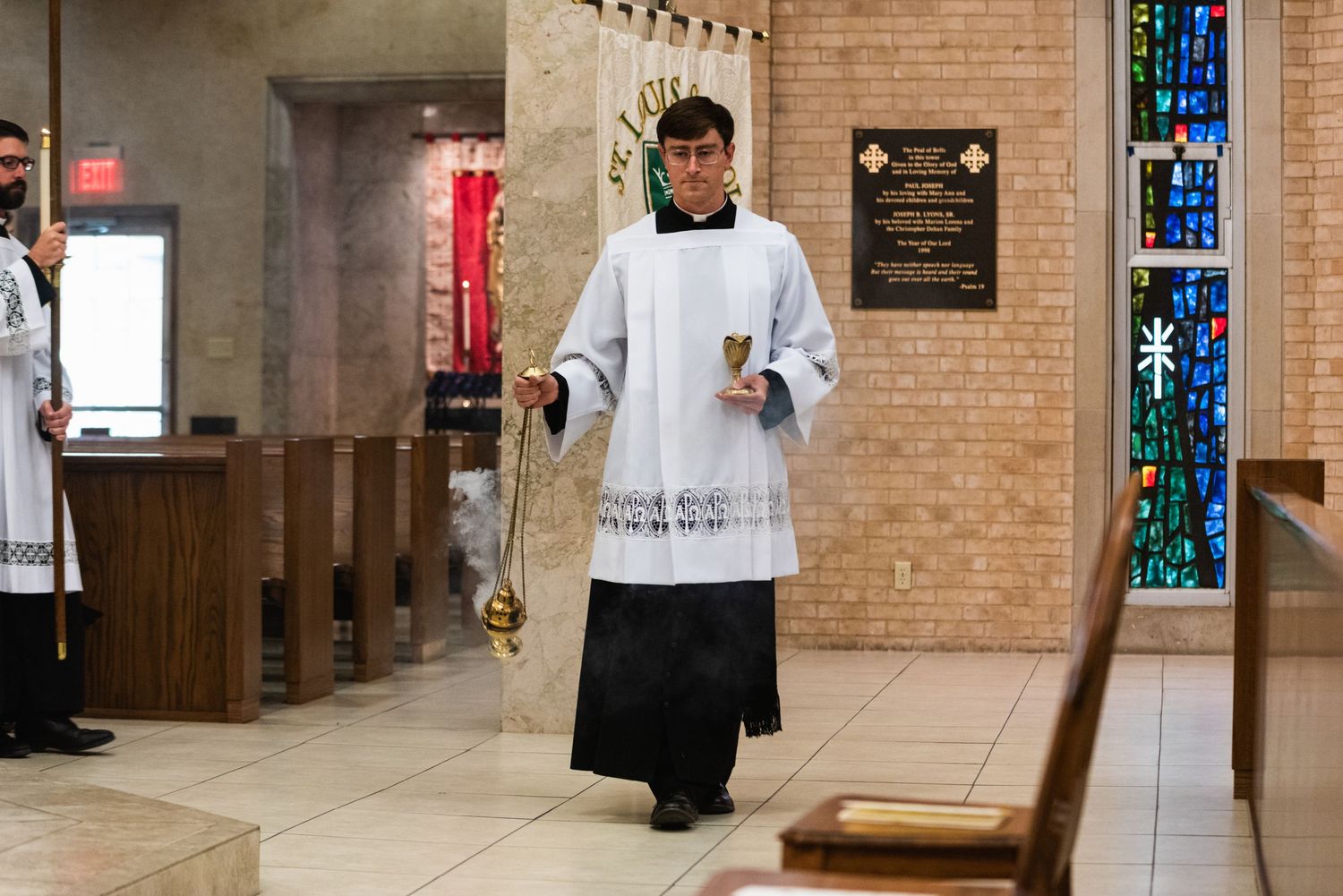Altar server in white robes walks down church aisle during religious ceremony.