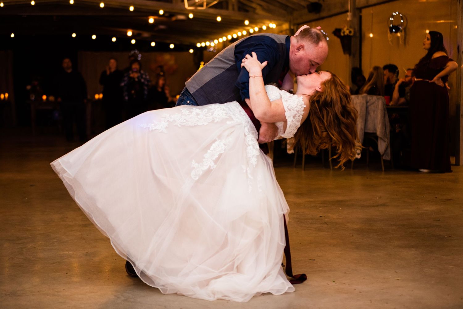 A dramatic wedding dance dip on a wooden dance floor under string lights.
