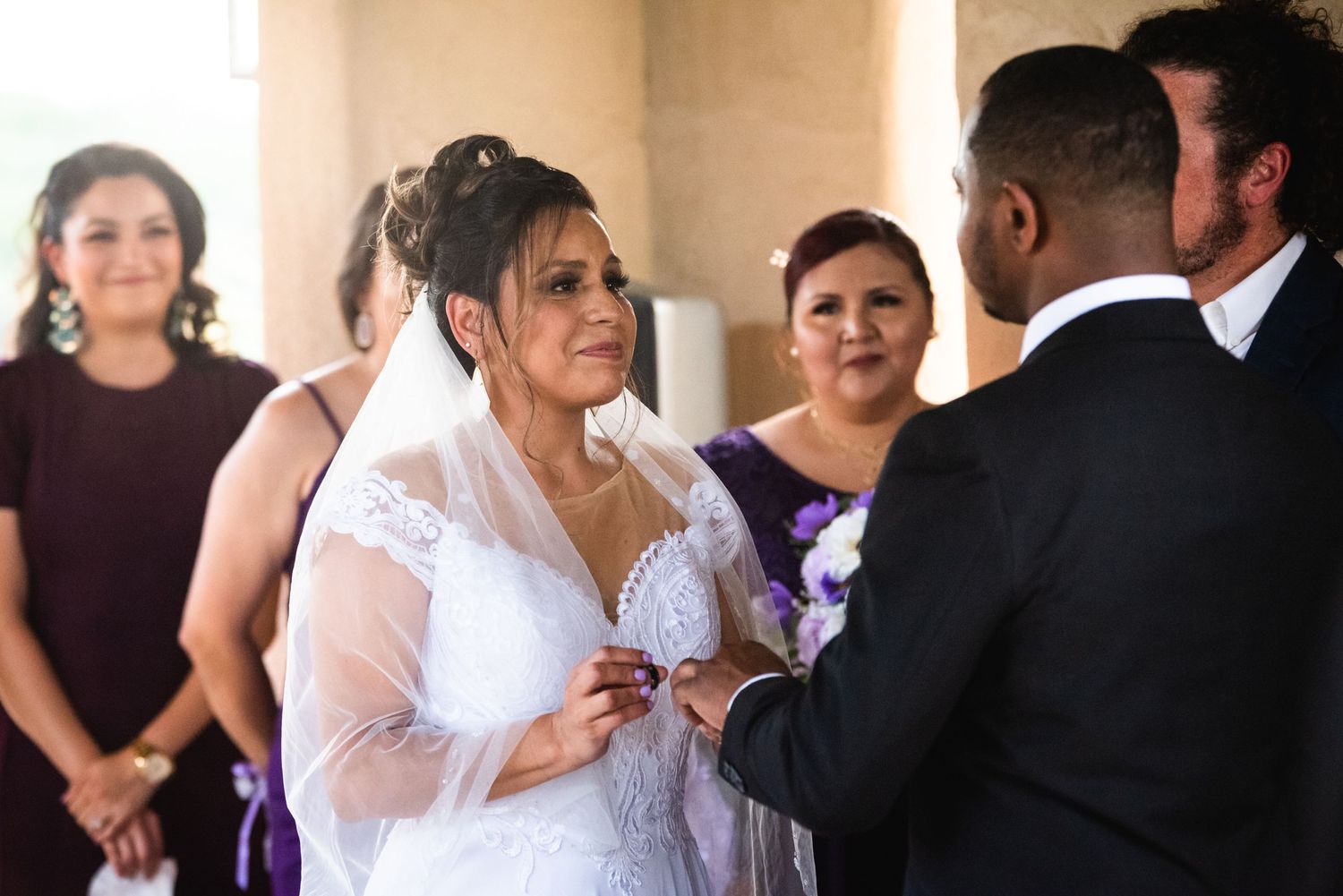 A tender moment during a wedding ceremony as vows are exchanged with bridesmaids looking on.