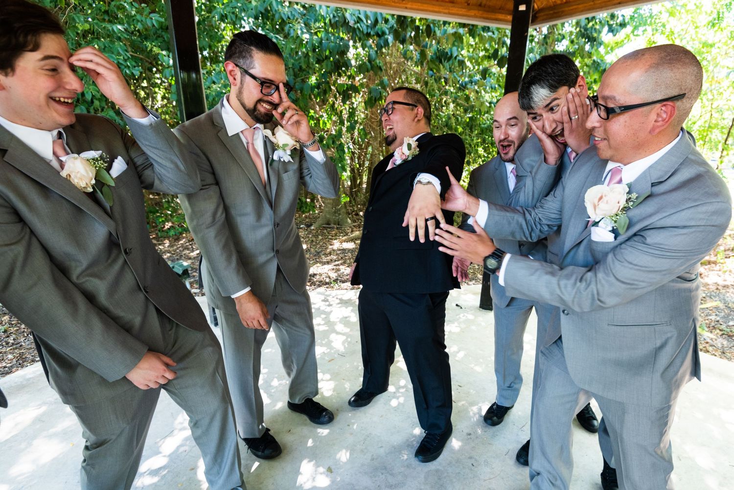 Groomsmen gather in grey suits under gazebo checking time on their watches.