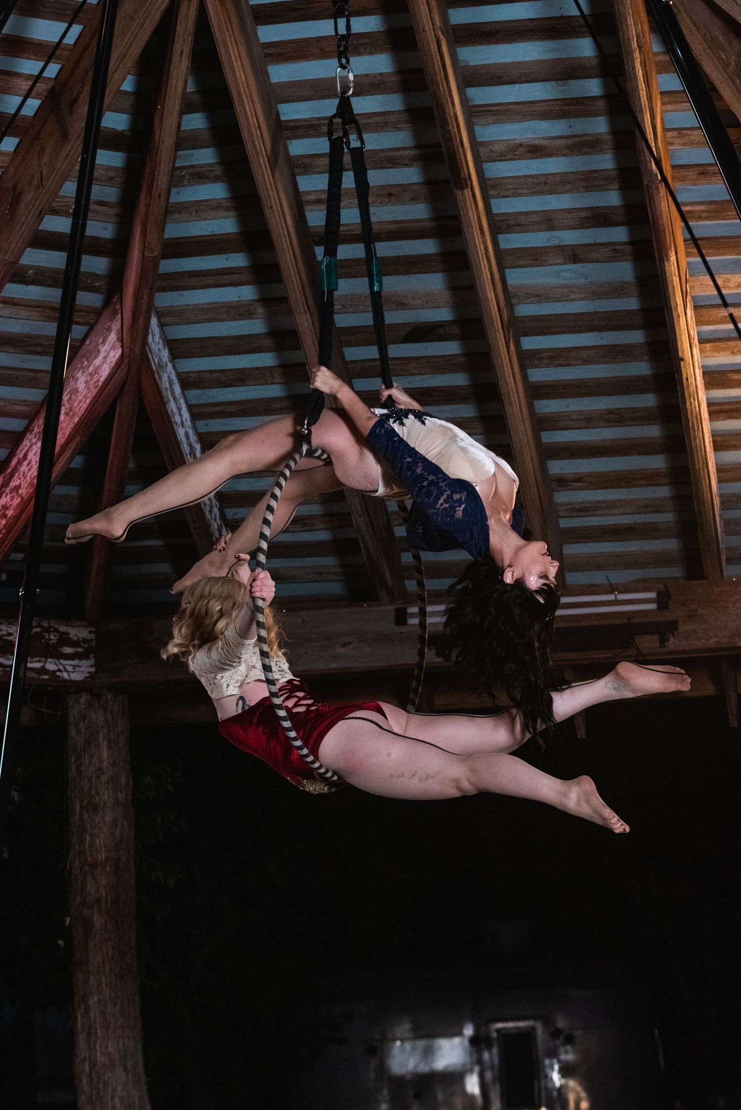 Aerial dancers perform synchronized moves while suspended from ropes in wooden structure.