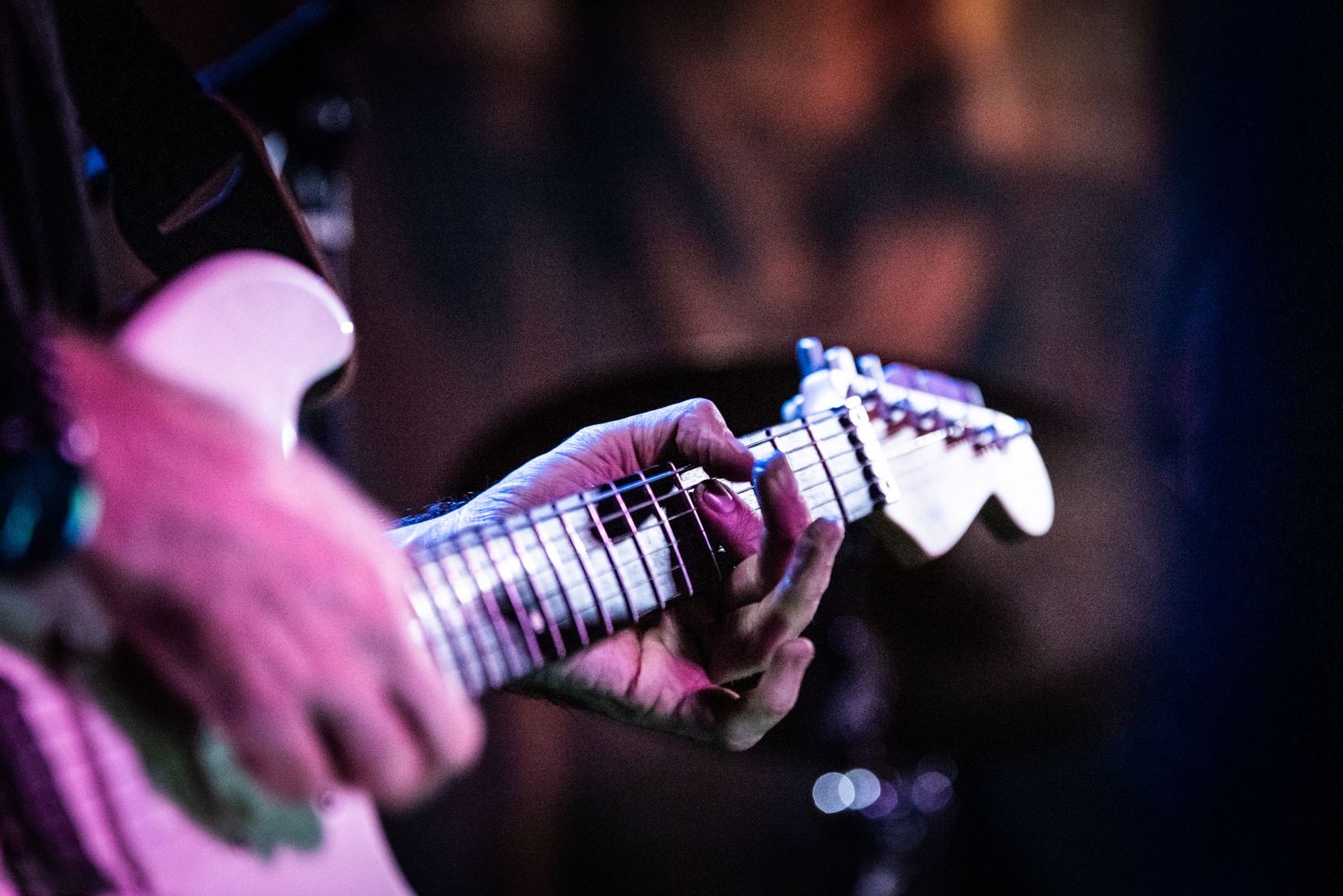 Close-up shot of hands playing an electric guitar with purple stage lighting.