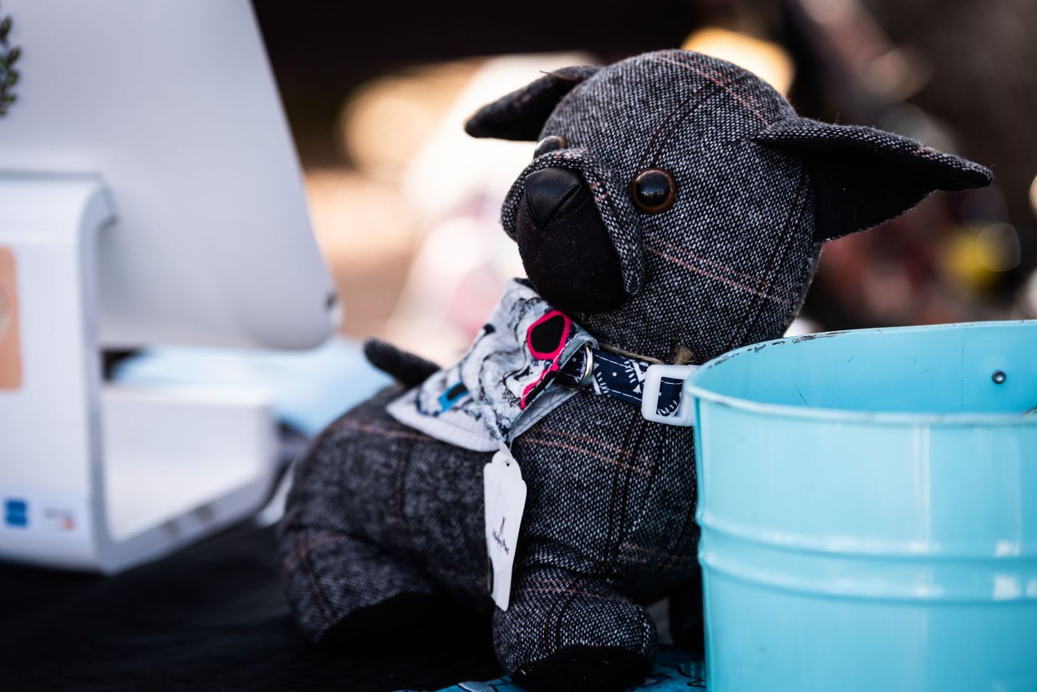 Gray plush dog toy with decorative bandana displayed at a craft market vendor booth.