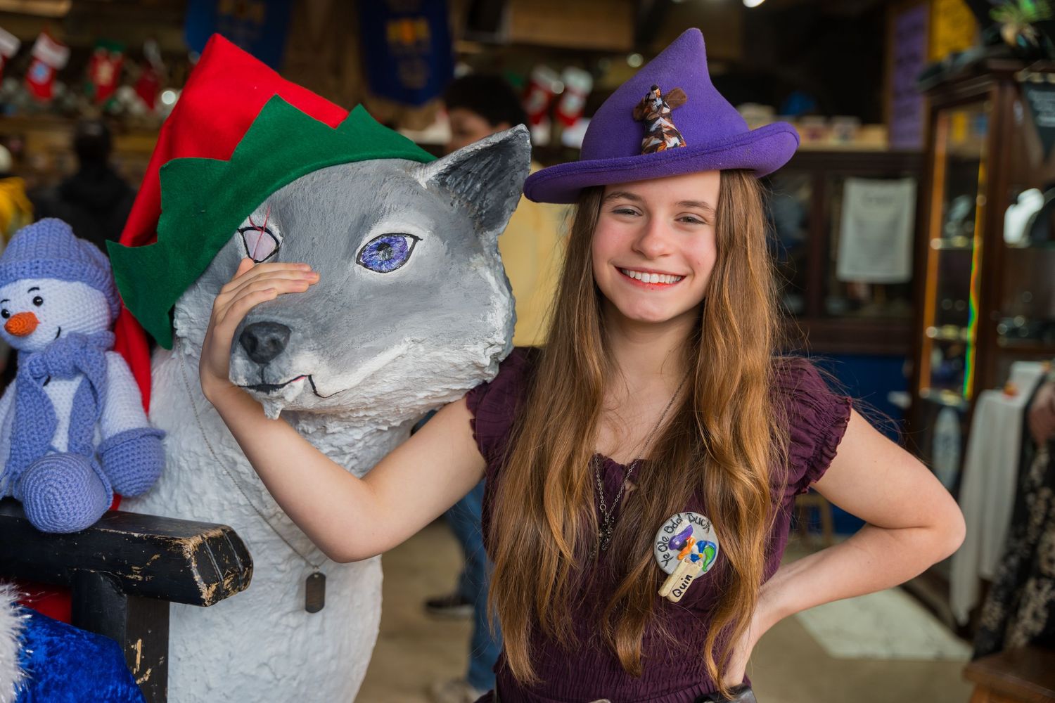 A person in a purple witch costume holding a wolf mask at a festival shop.