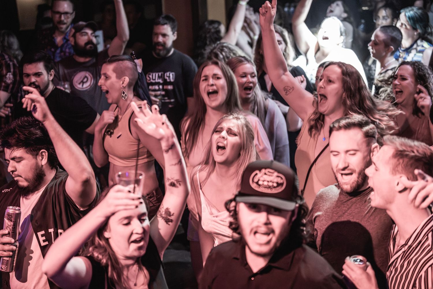 An enthusiastic crowd cheers with raised arms during a live music performance.