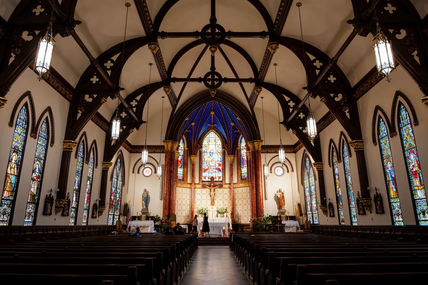 Interior view of a gothic church sanctuary with vaulted wooden arches, stained glass windows and a dramatic blue altar.