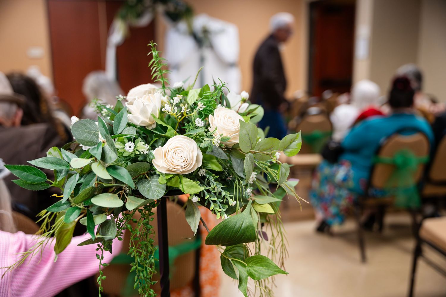 Wedding floral centerpiece with cream roses and greenery on display at an indoor event space.