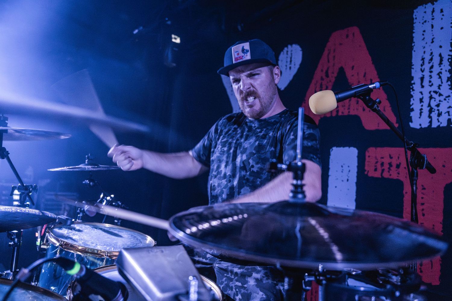 Energetic drummer performing with dramatic blue lighting during live concert.