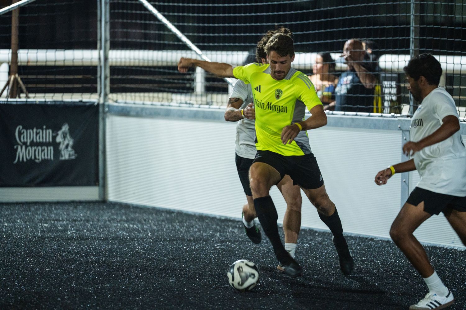 Soccer players battle for possession on an illuminated indoor court at night.