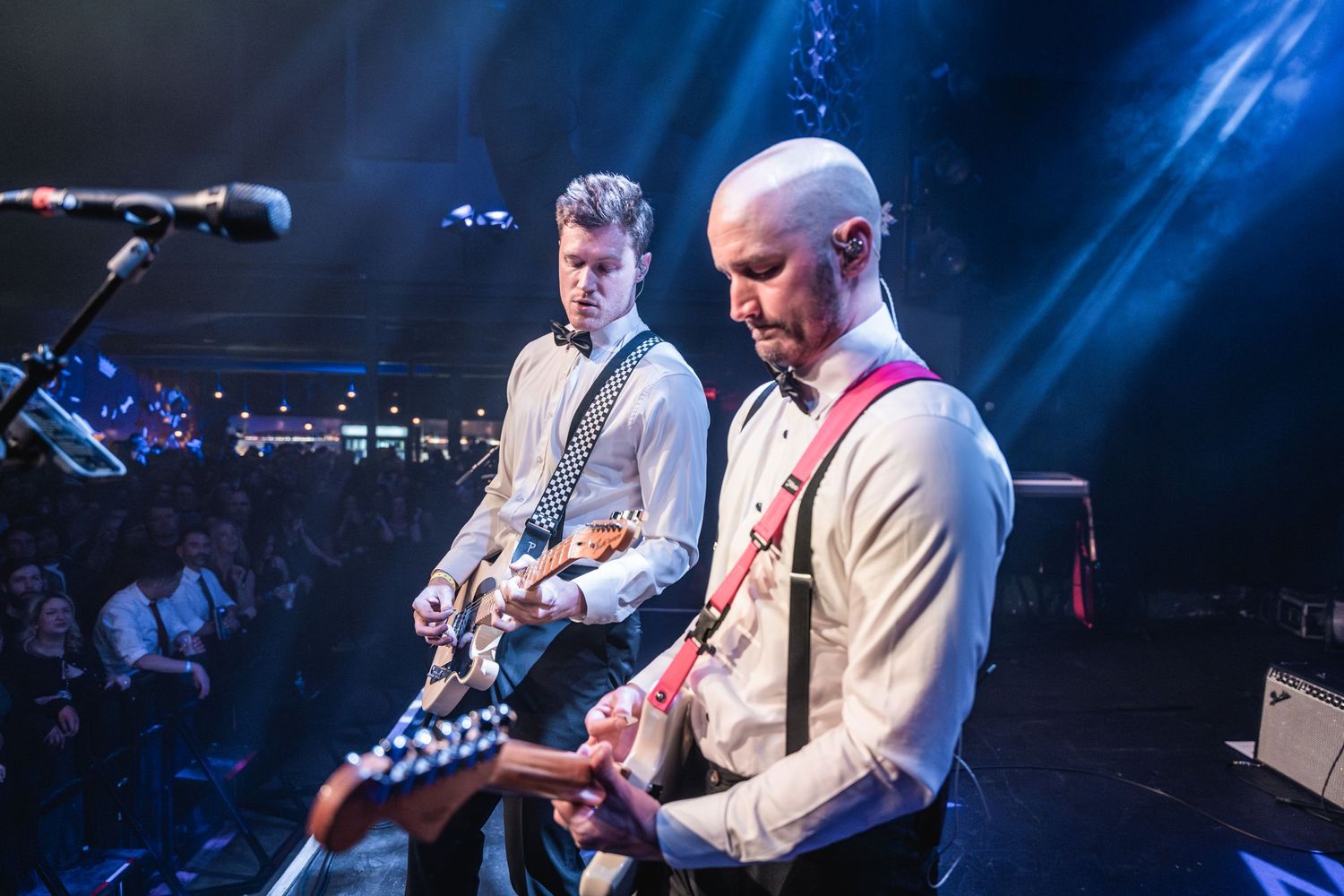 Musicians performing on stage with dramatic blue spotlights and guitar equipment.