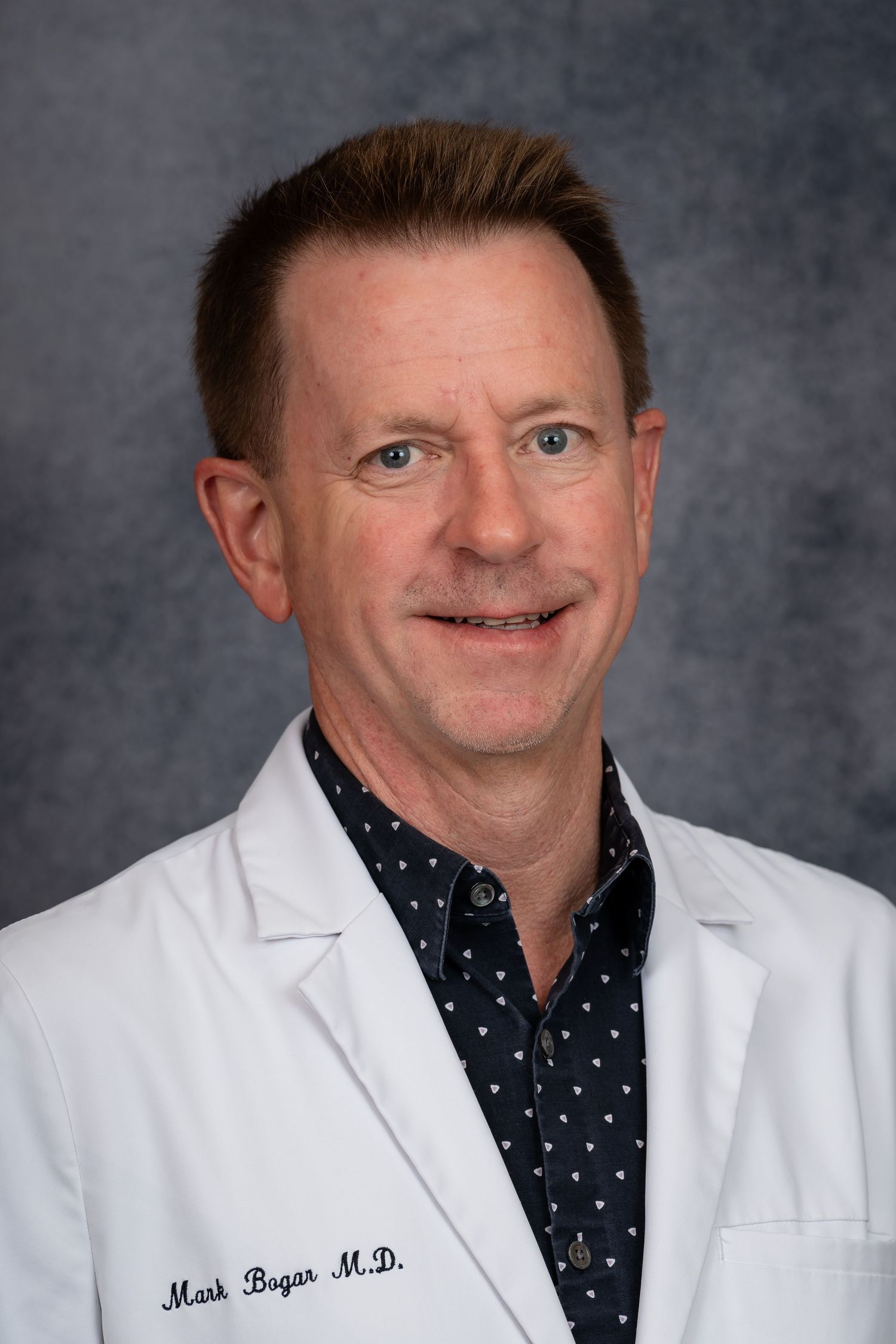 Healthcare professional in white coat and polka dot shirt poses for headshot.