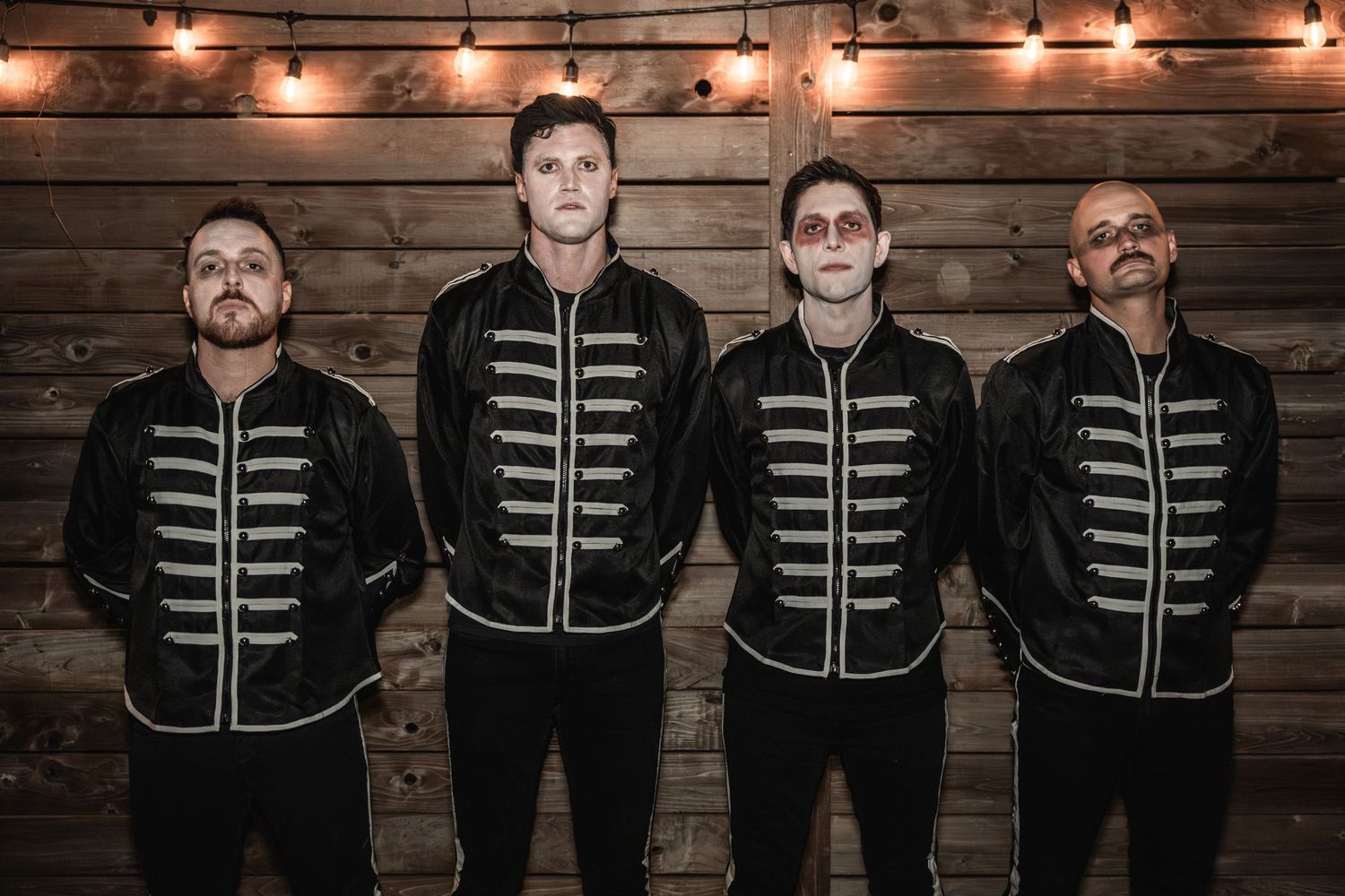 Four musicians stand in formation wearing coordinated black military-inspired uniforms.