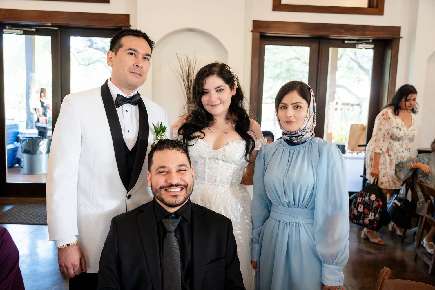 Wedding party gathered together at an elegant indoor venue with white walls and arched windows.