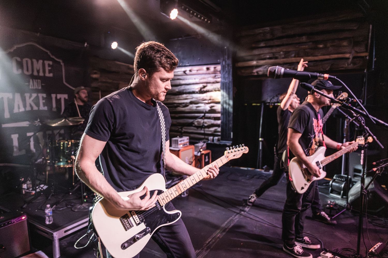 Musicians playing electric guitars during rock performance on dimly lit stage.