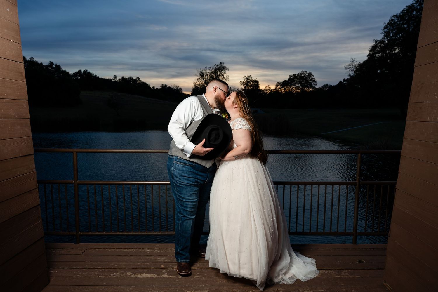 Romantic nighttime portrait of newlyweds on a deck overlooking a lake at twilight.