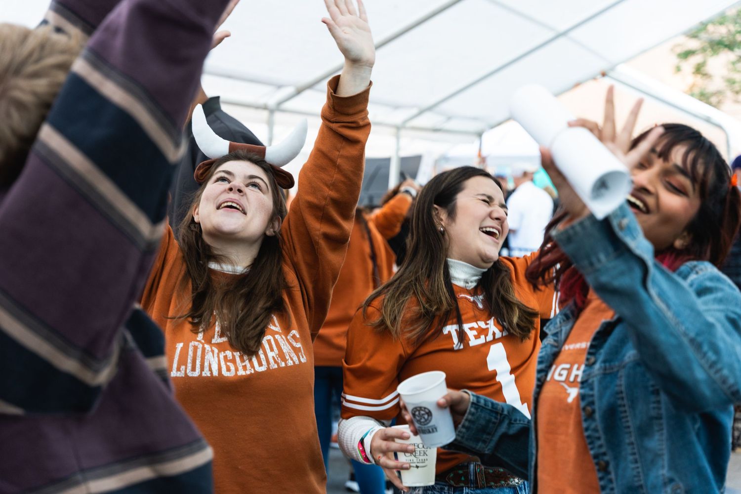 Students cheering enthusiastically at an outdoor event wearing matching orange university sweatshirts.