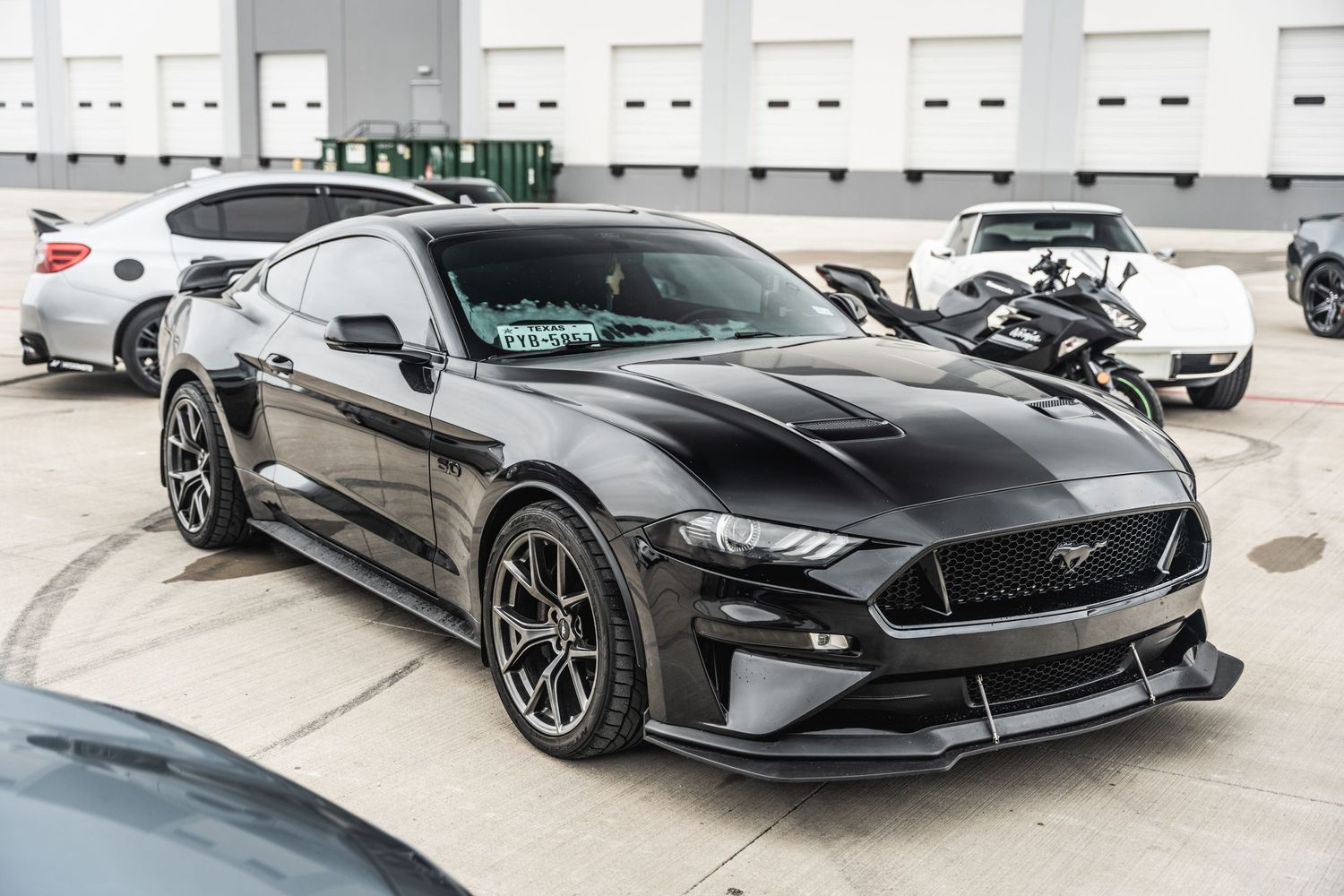 Black Ford Mustang with custom wheels and aerodynamic modifications parked in lot.