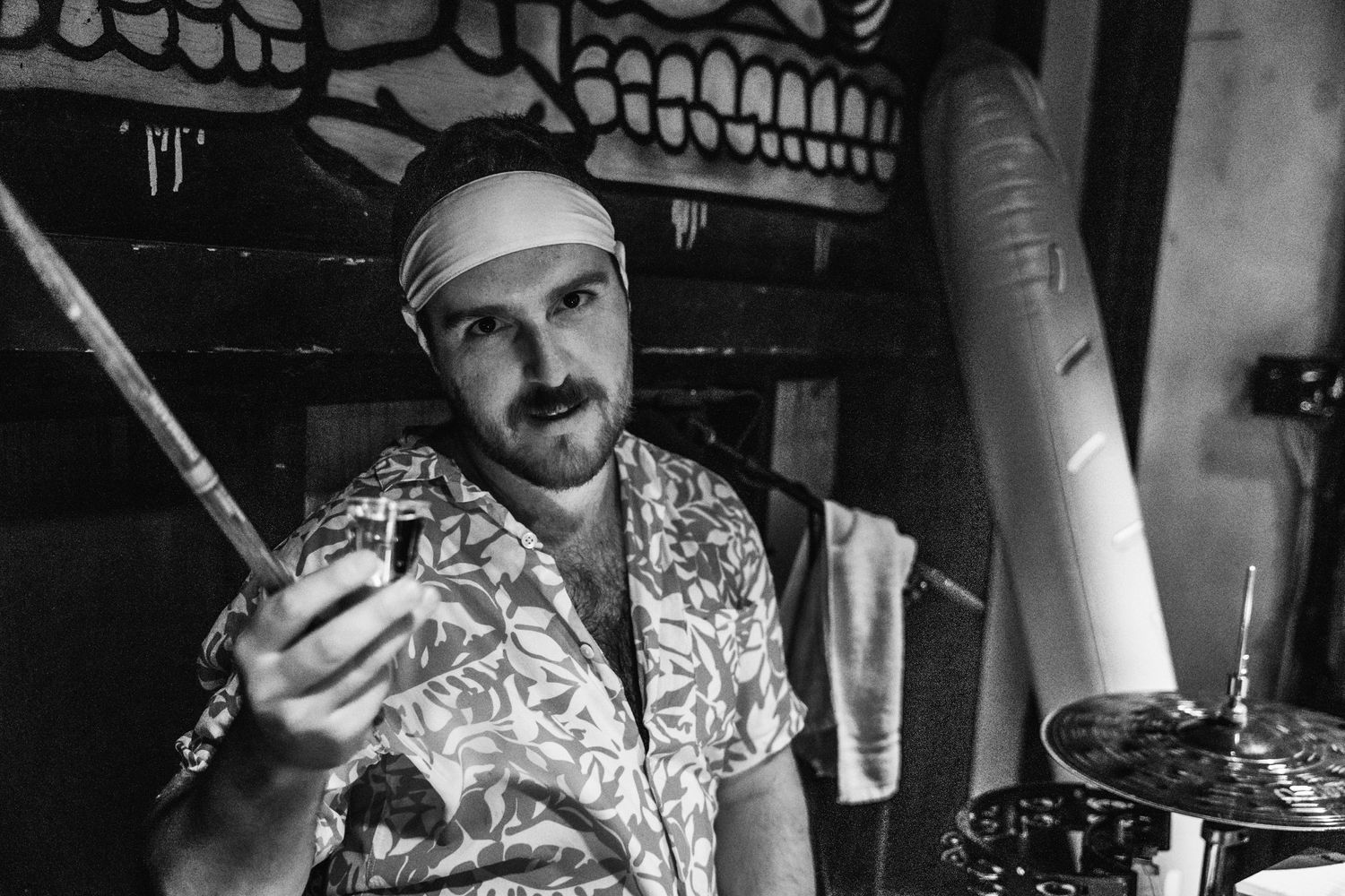 Black and white photo of person in patterned shirt examining something in dark setting.