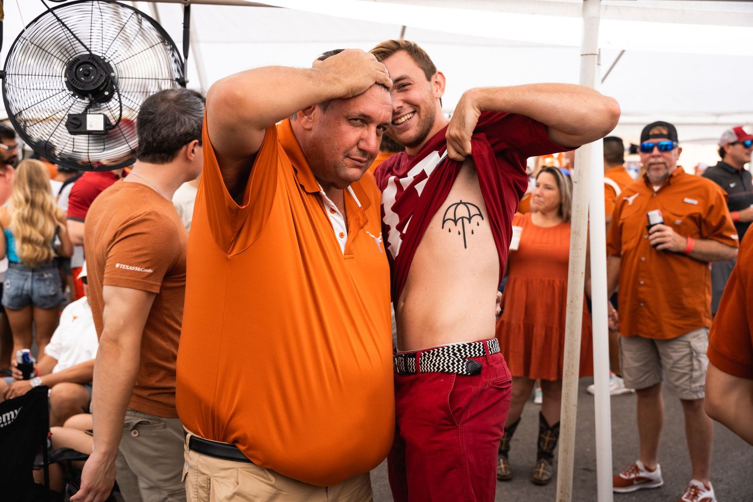 Two people pose together under a white tent at a casual outdoor gathering.