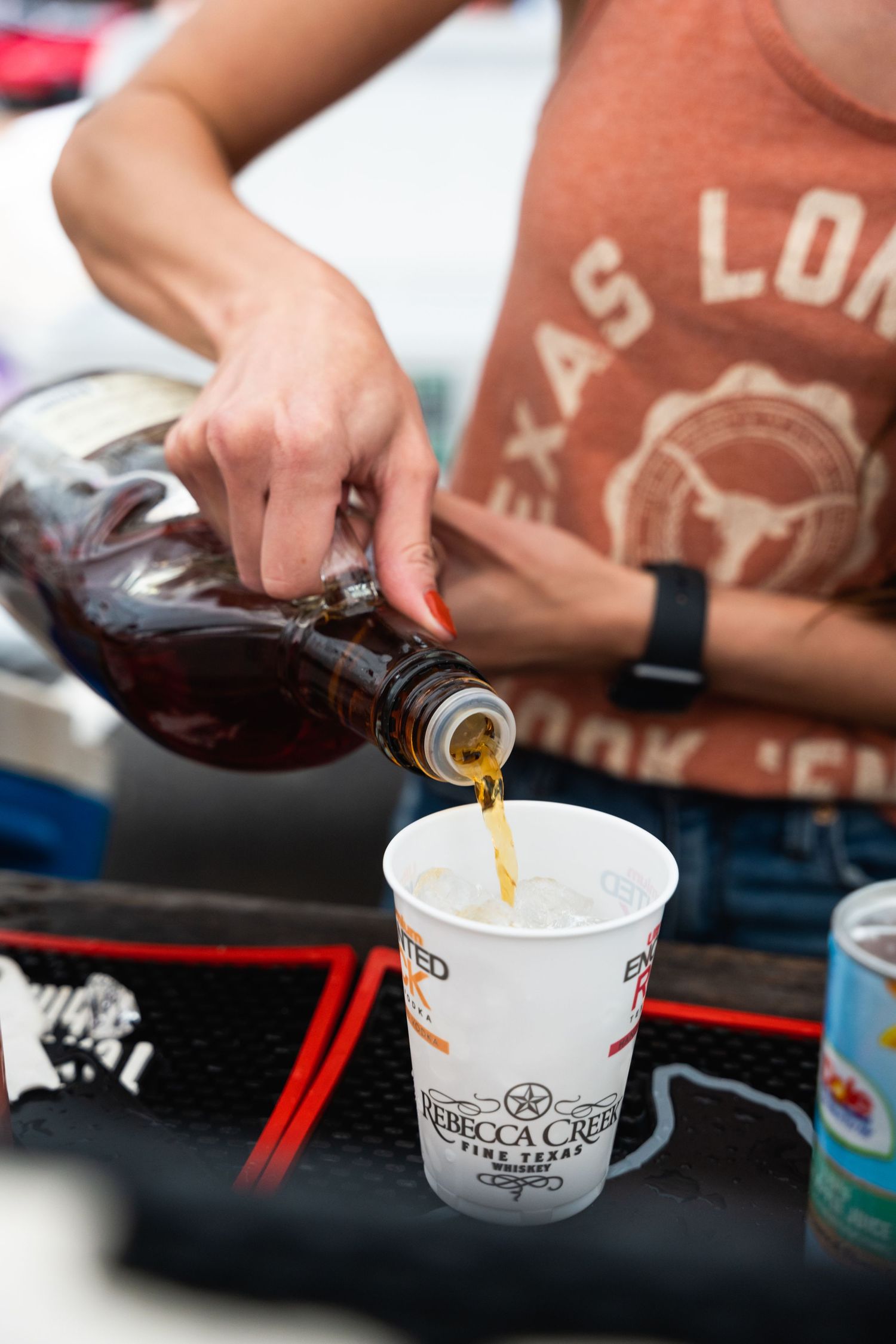 Someone pouring a dark beverage into a branded cup at an outdoor event.
