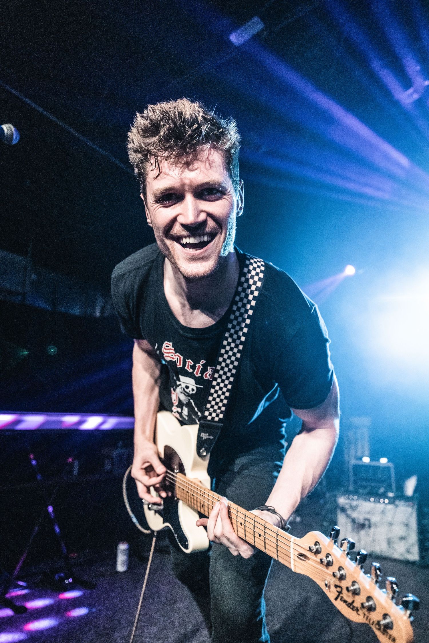 Musician playing electric guitar with enthusiastic expression under blue stage lights.