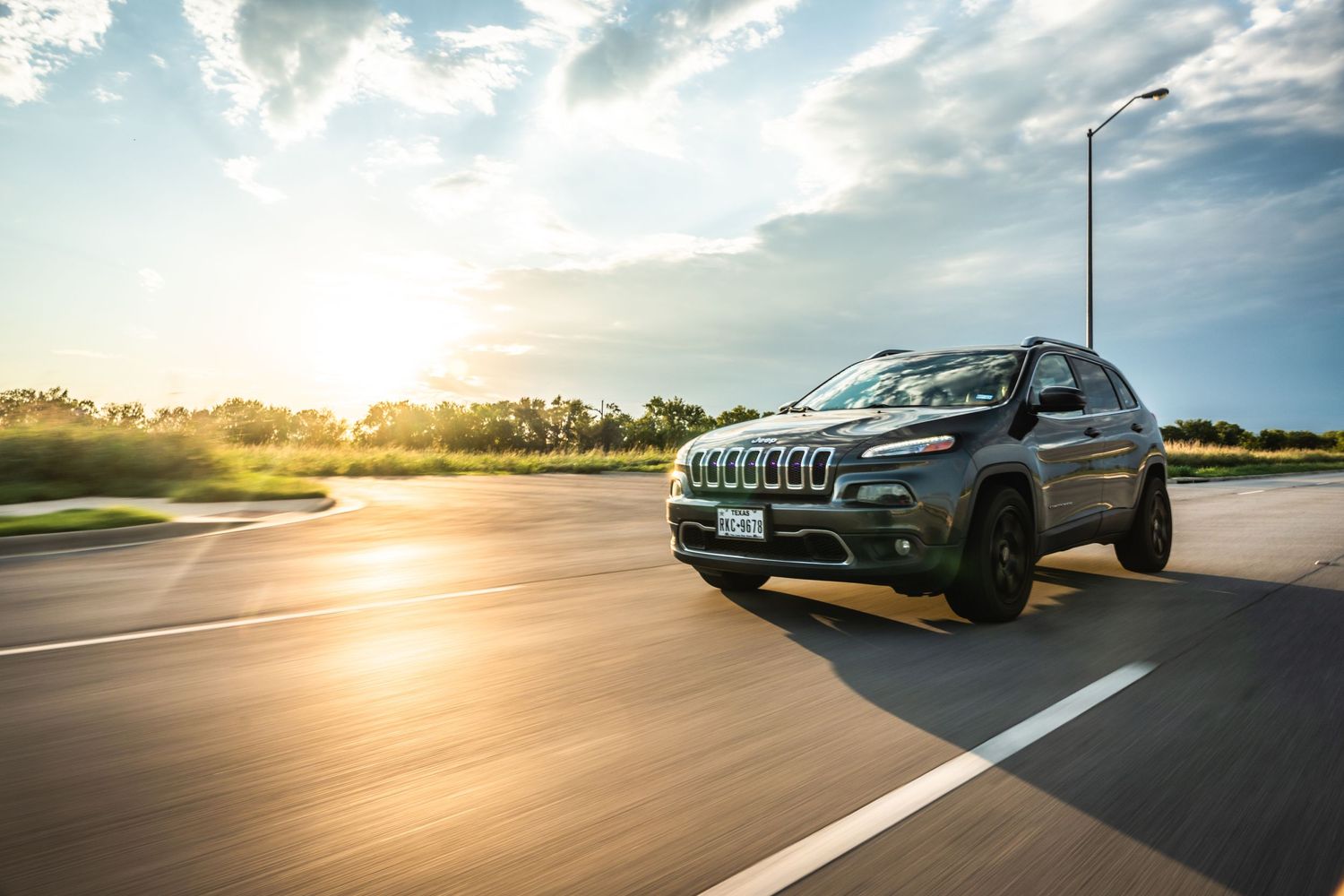 Jeep Cherokee with black accents captured during golden hour on open road.