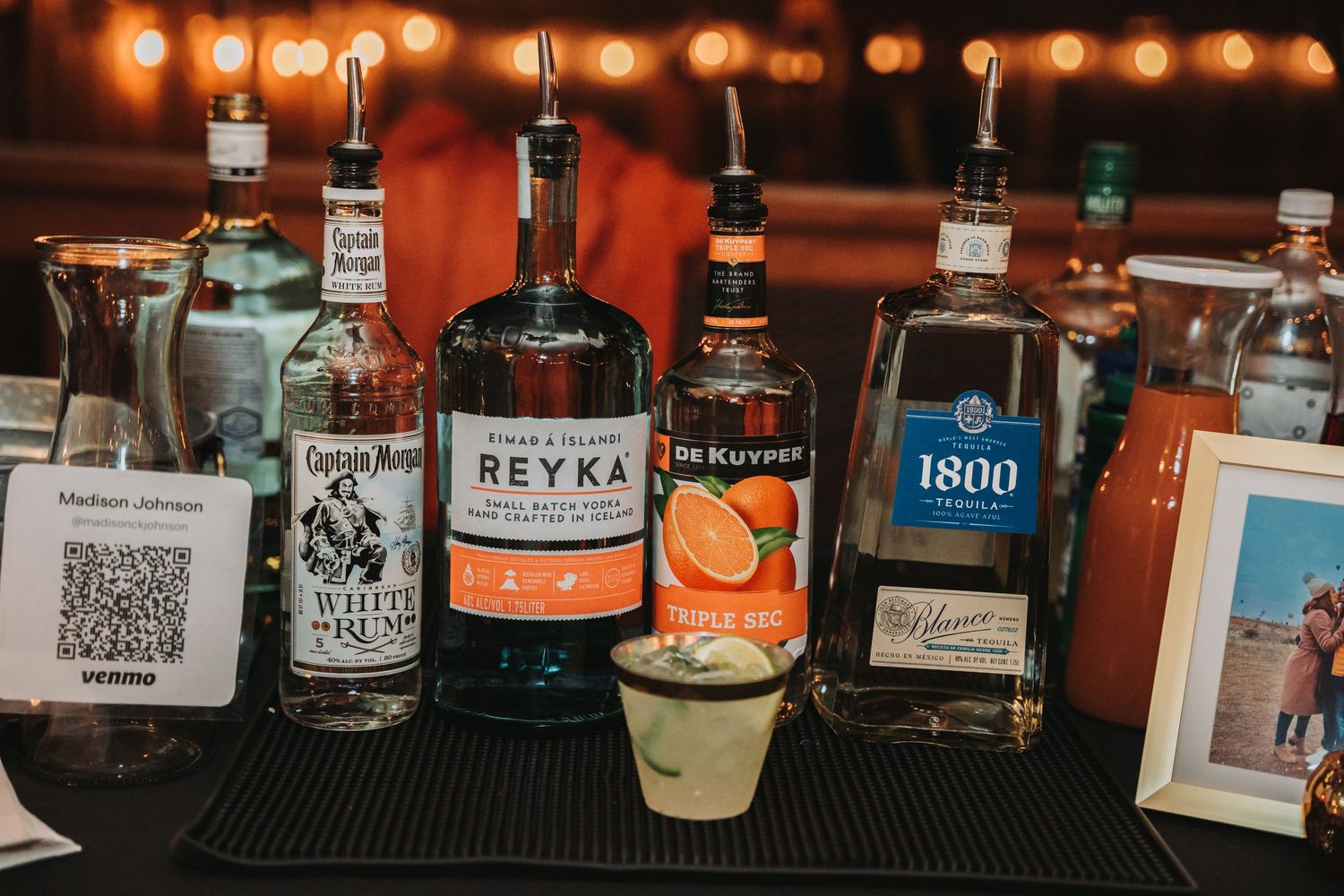 Bar display featuring various liquor bottles including Reyka vodka and 1800 tequila with ambient lighting.