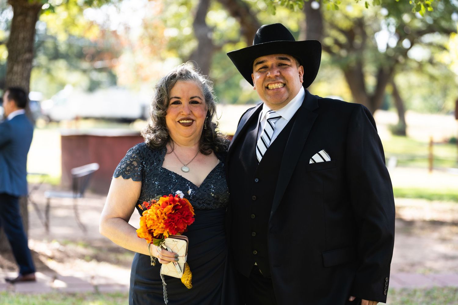 A couple in formal western attire poses during an outdoor event with orange flowers.