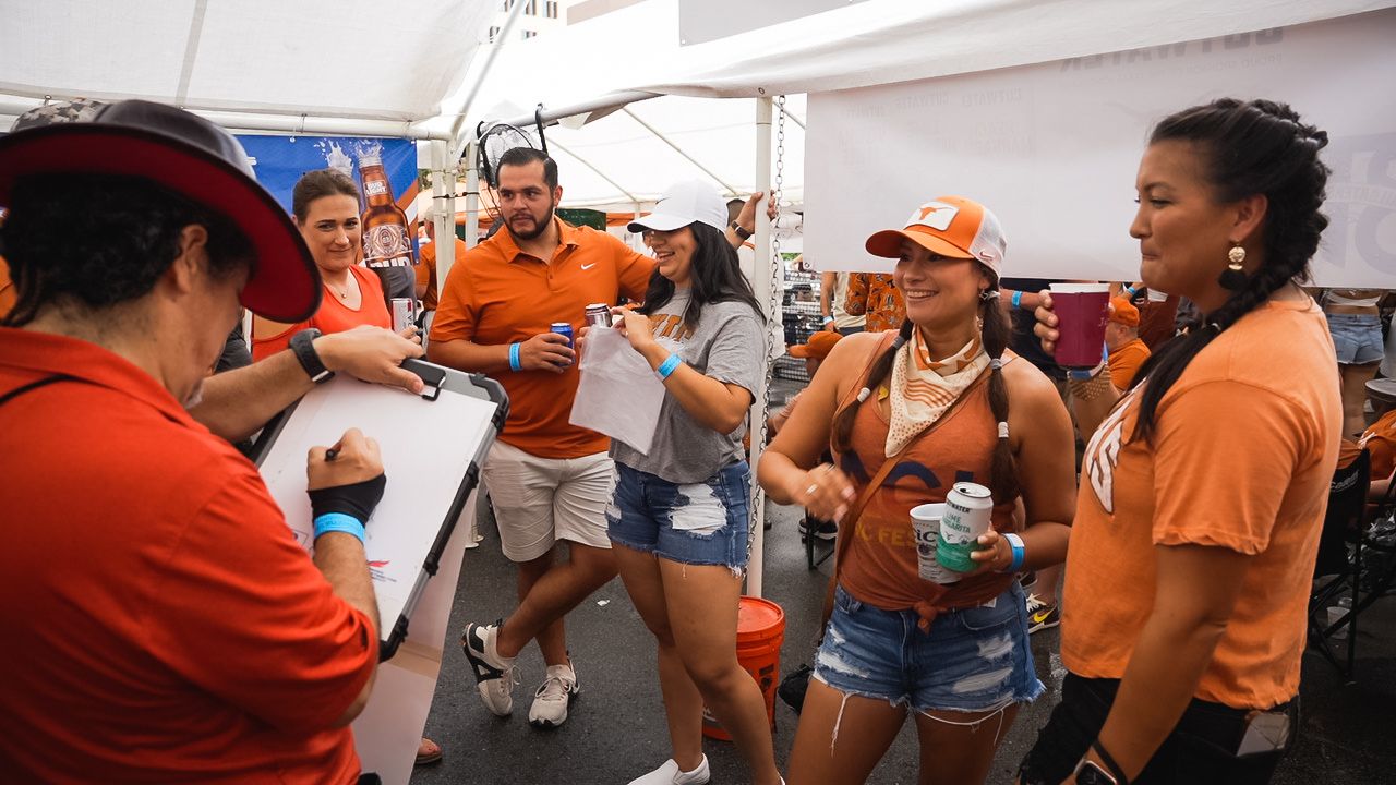 Festive crowd in orange attire socializing at outdoor event under white tent.