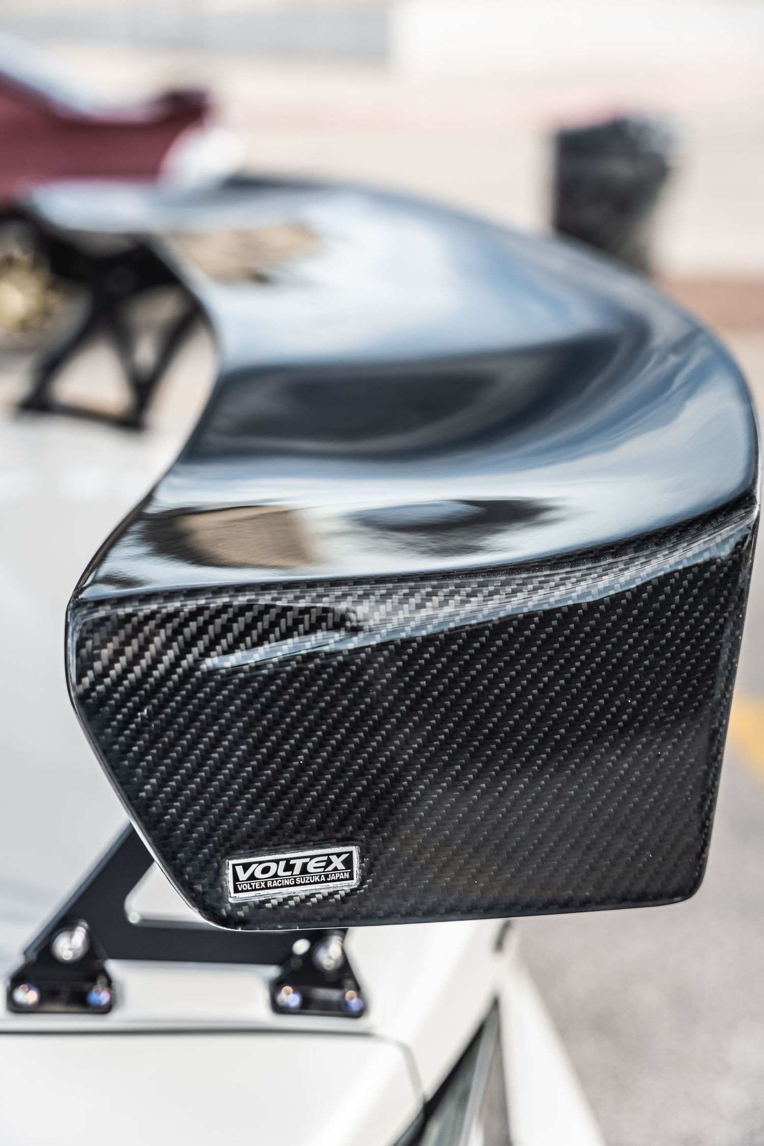 Detail shot of a glossy black carbon fiber Voltex automotive wing or spoiler.