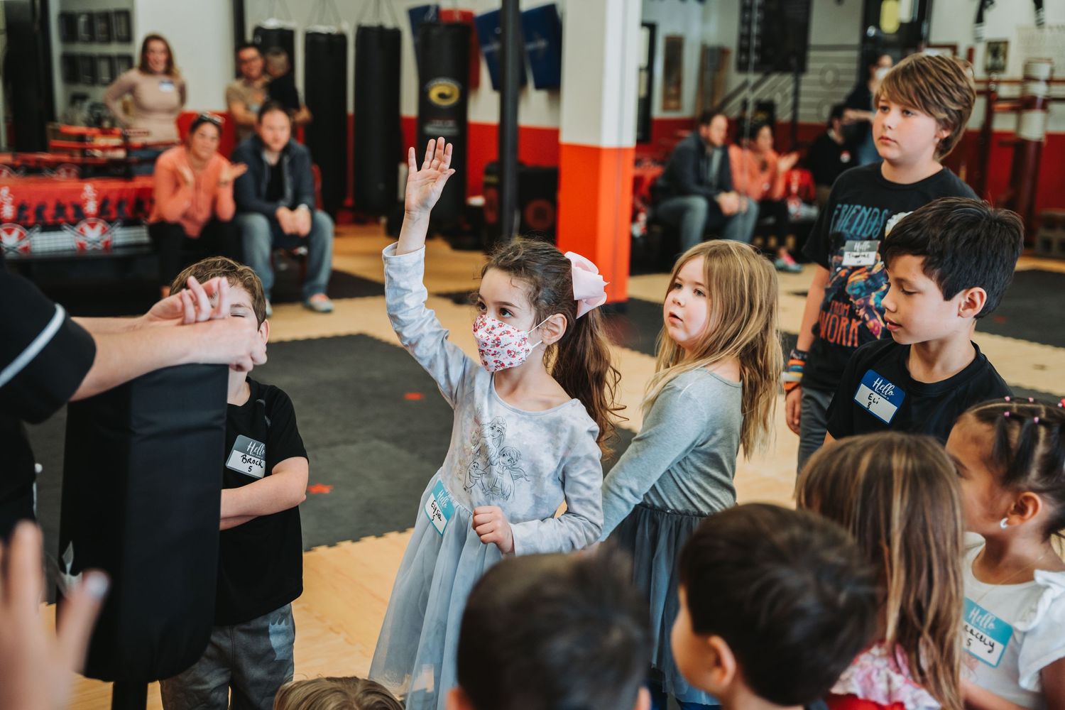 Students raising hands during interactive martial arts class session.