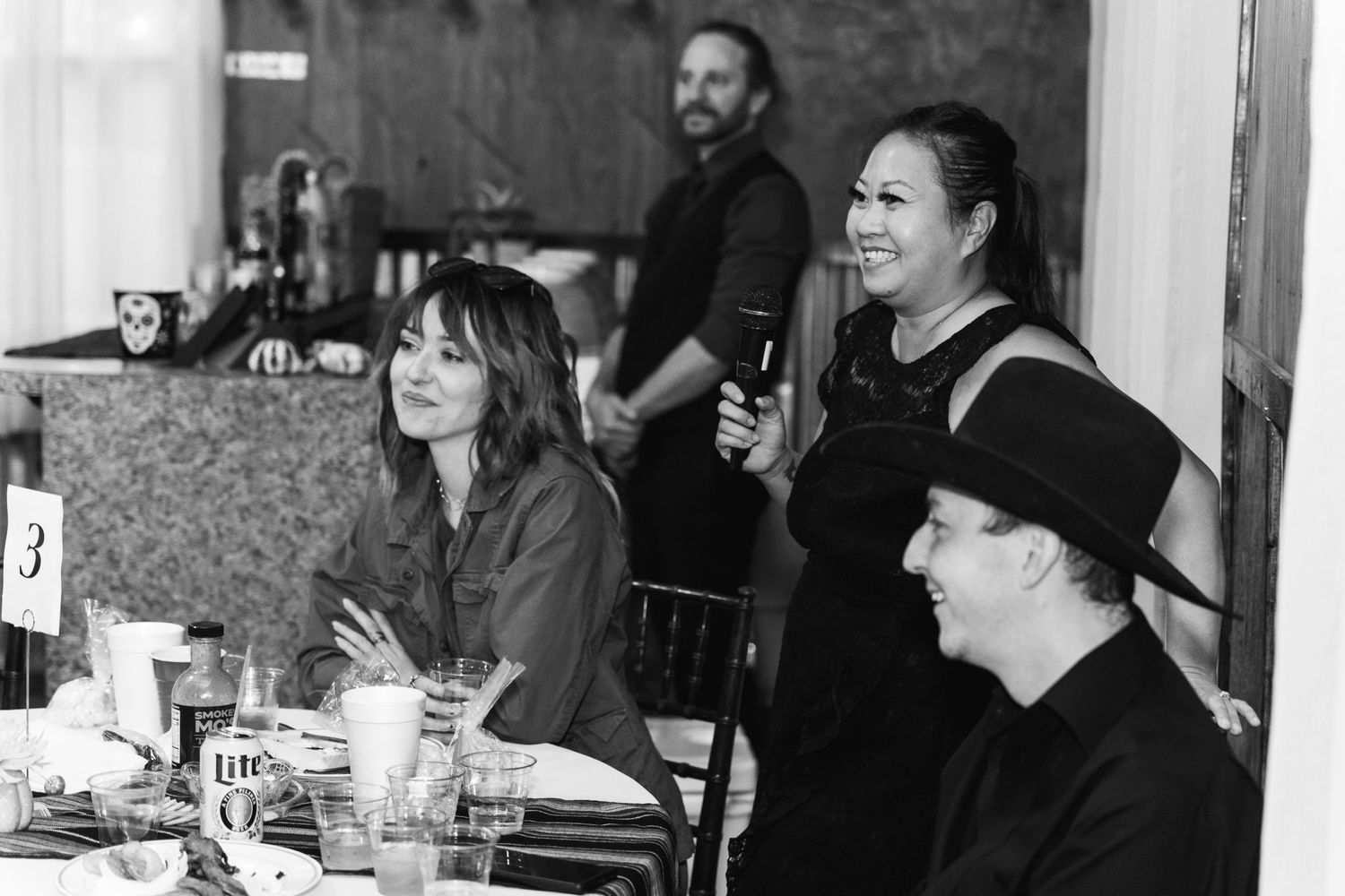 A casual black and white photo of people gathered around a table in conversation.