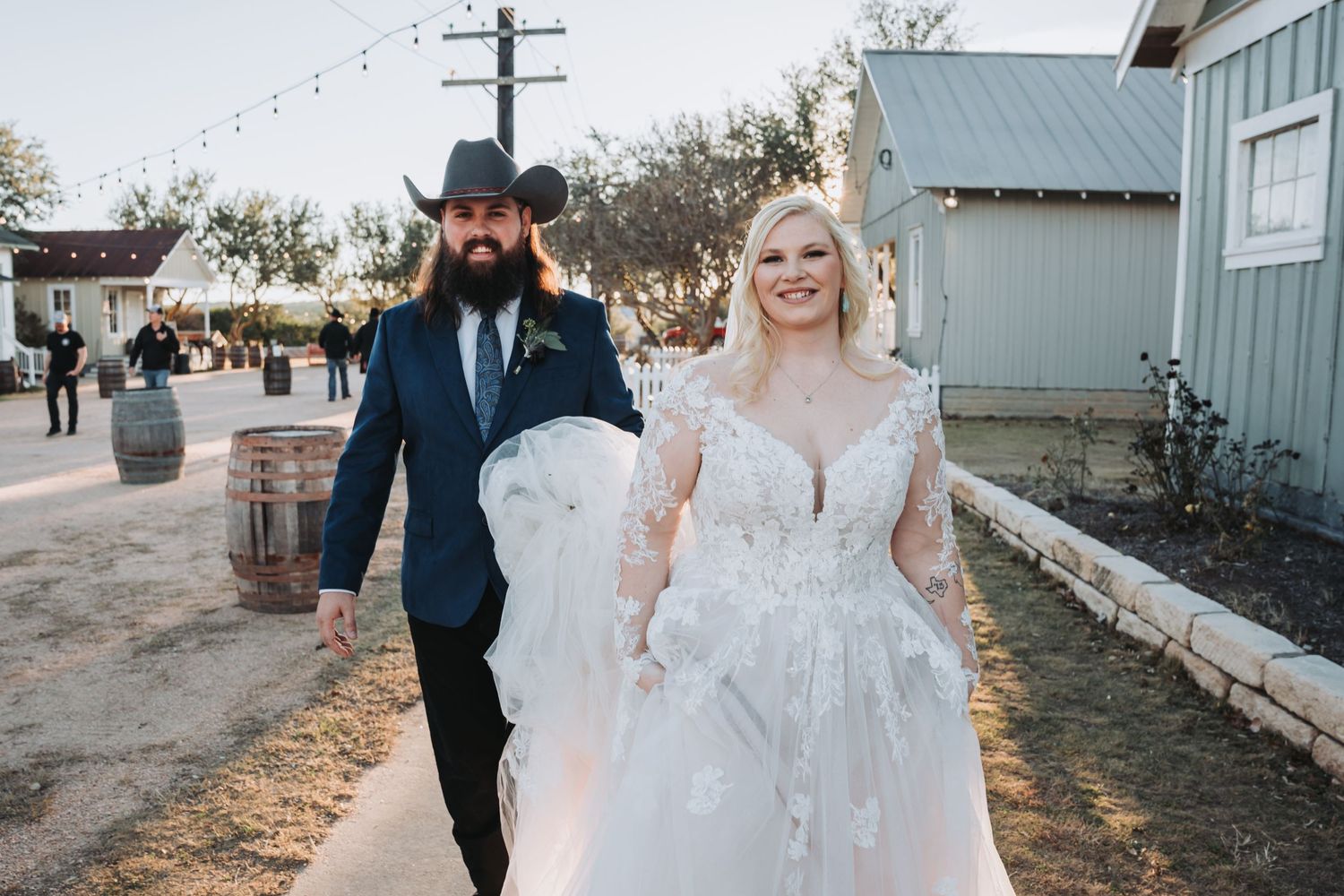 A couple walks together outdoors during their wedding celebration with string lights overhead.